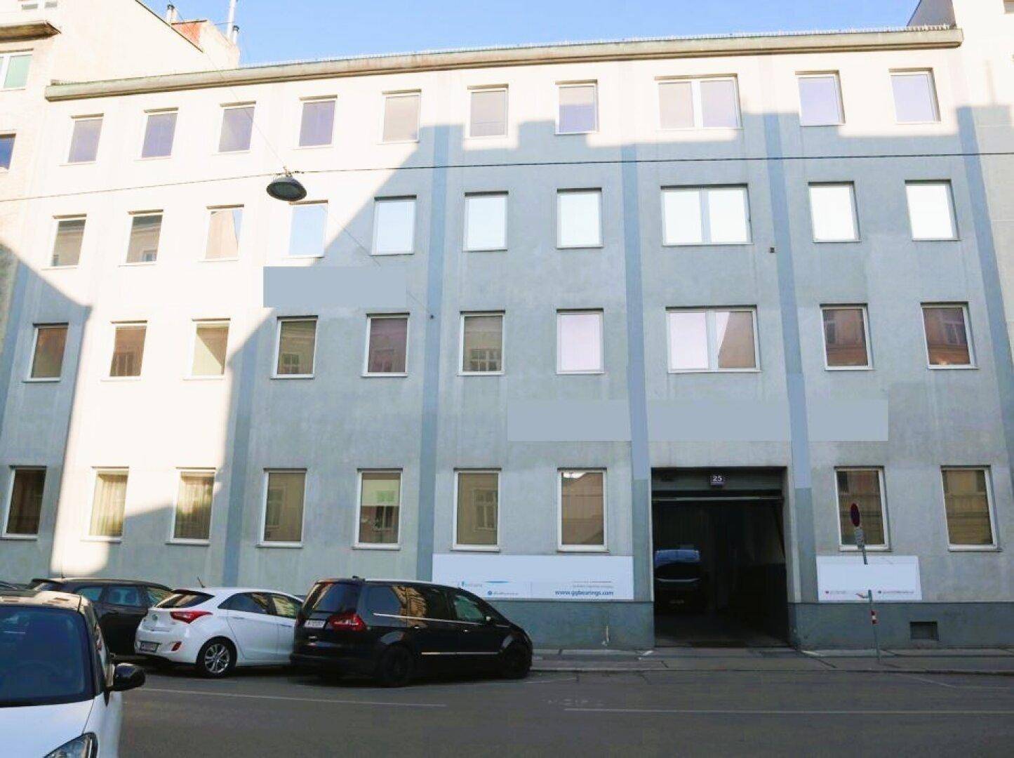 Fassade eines mehrstöckigen Gebäudes mit vielen Fenstern und einem großen Eingangsbereich im Erdgeschoss.