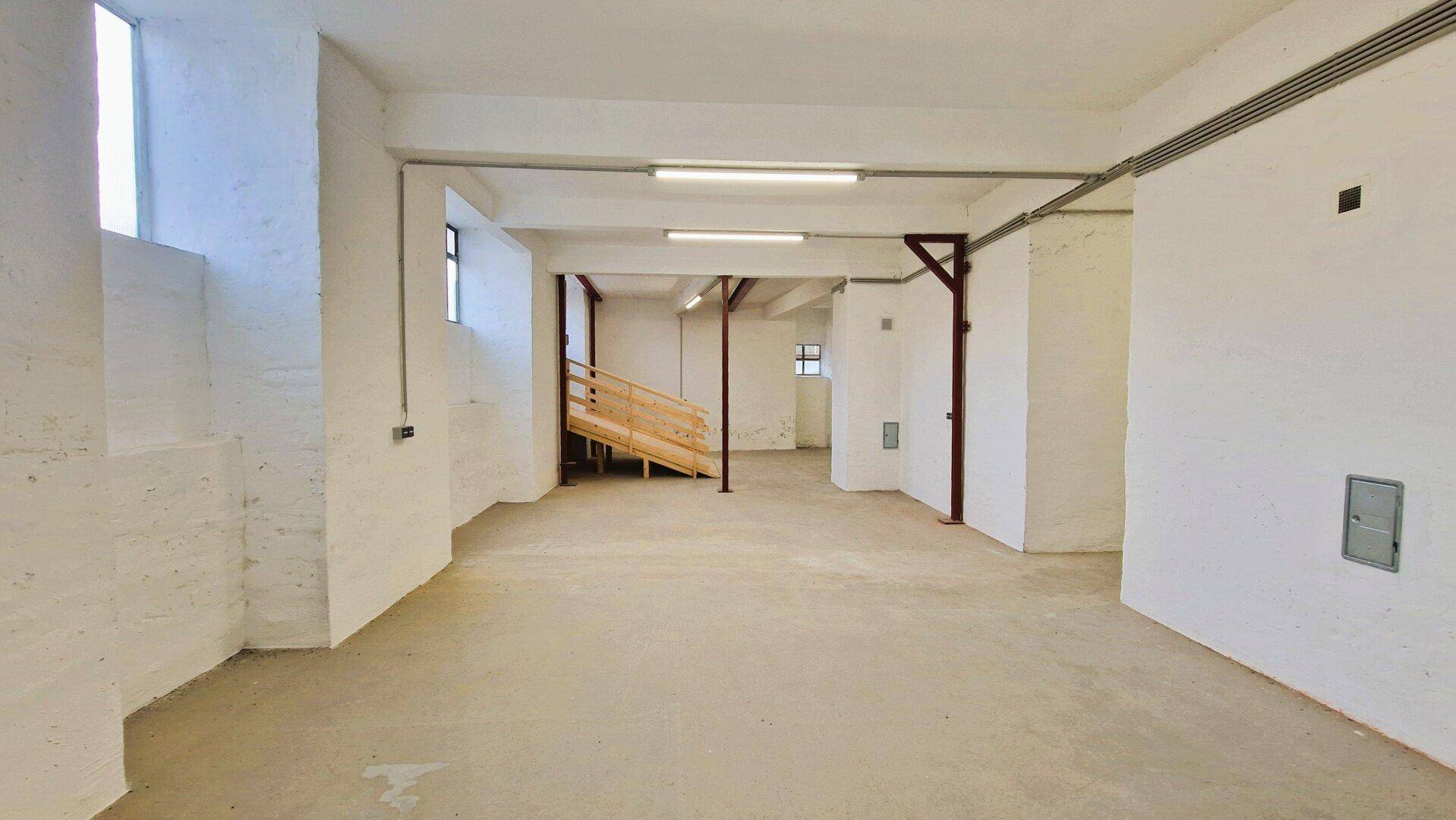 Weitläufiger Lagerraum mit Betonboden, weißen Wänden, hohen Decken und einer Rampe in der Ferne.