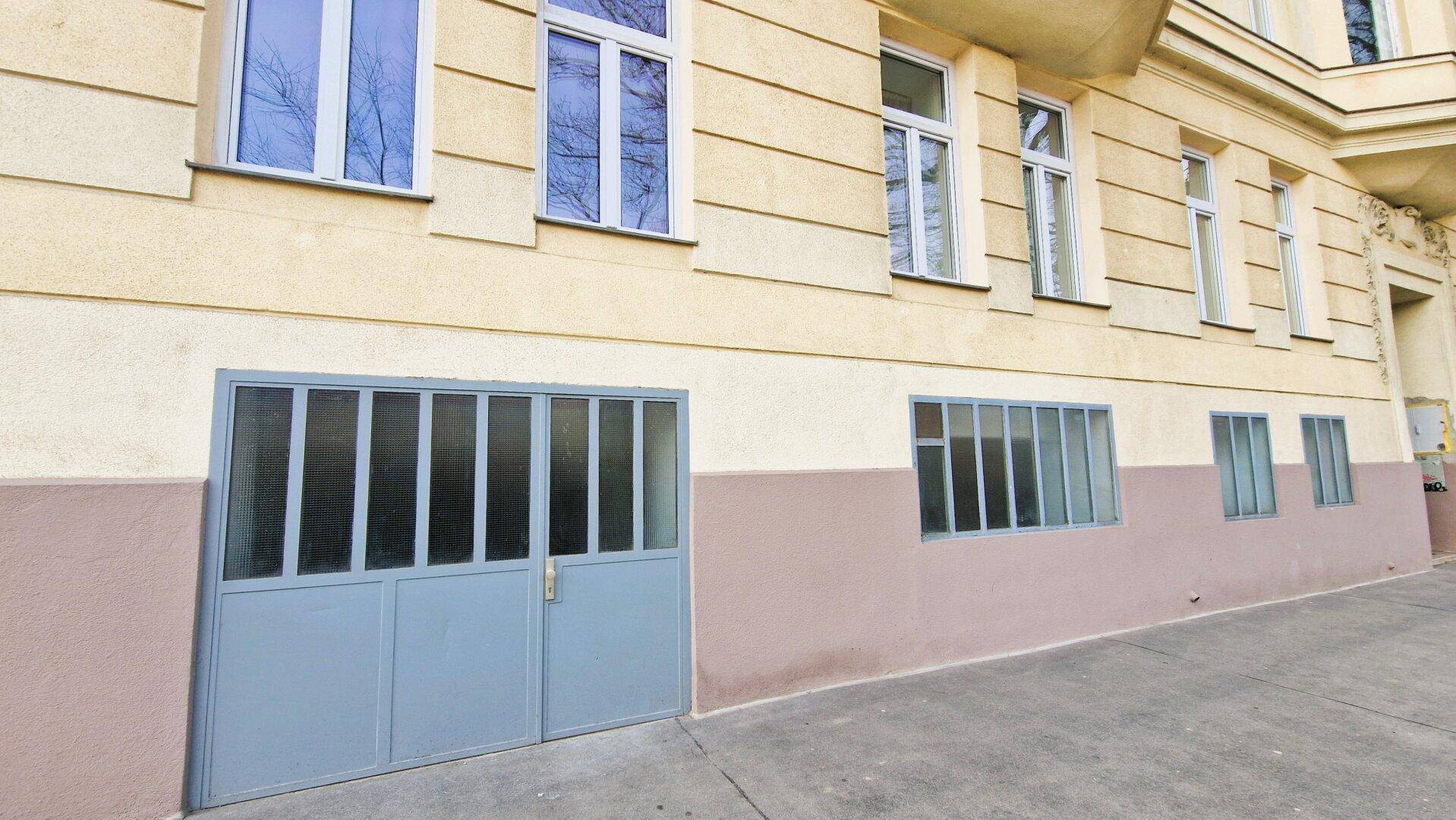 Nahaufnahme der gelben Gebäudefassade mit einem großen blauen Garagentor und mehreren Fenstern auf Straßenniveau.