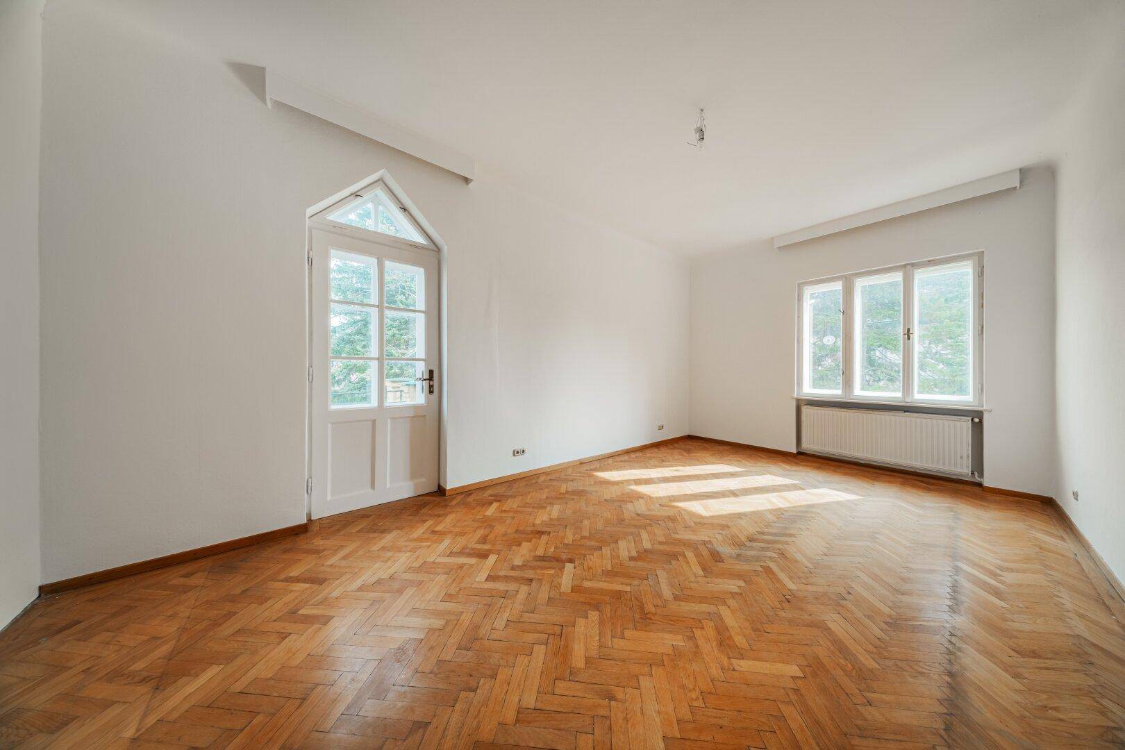 Heller Raum mit Fischgrätparkett, Zugang zu einem Außenbereich und großem Fenster.