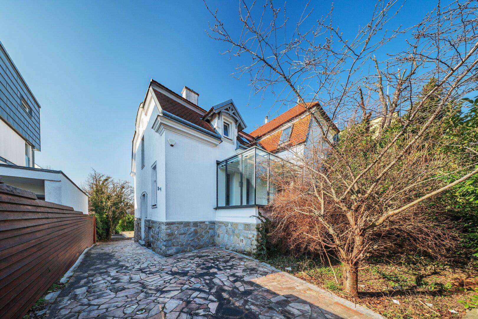 Seitenansicht des Hauses mit gepflasterter Auffahrt und einem modernen Glasanbau.