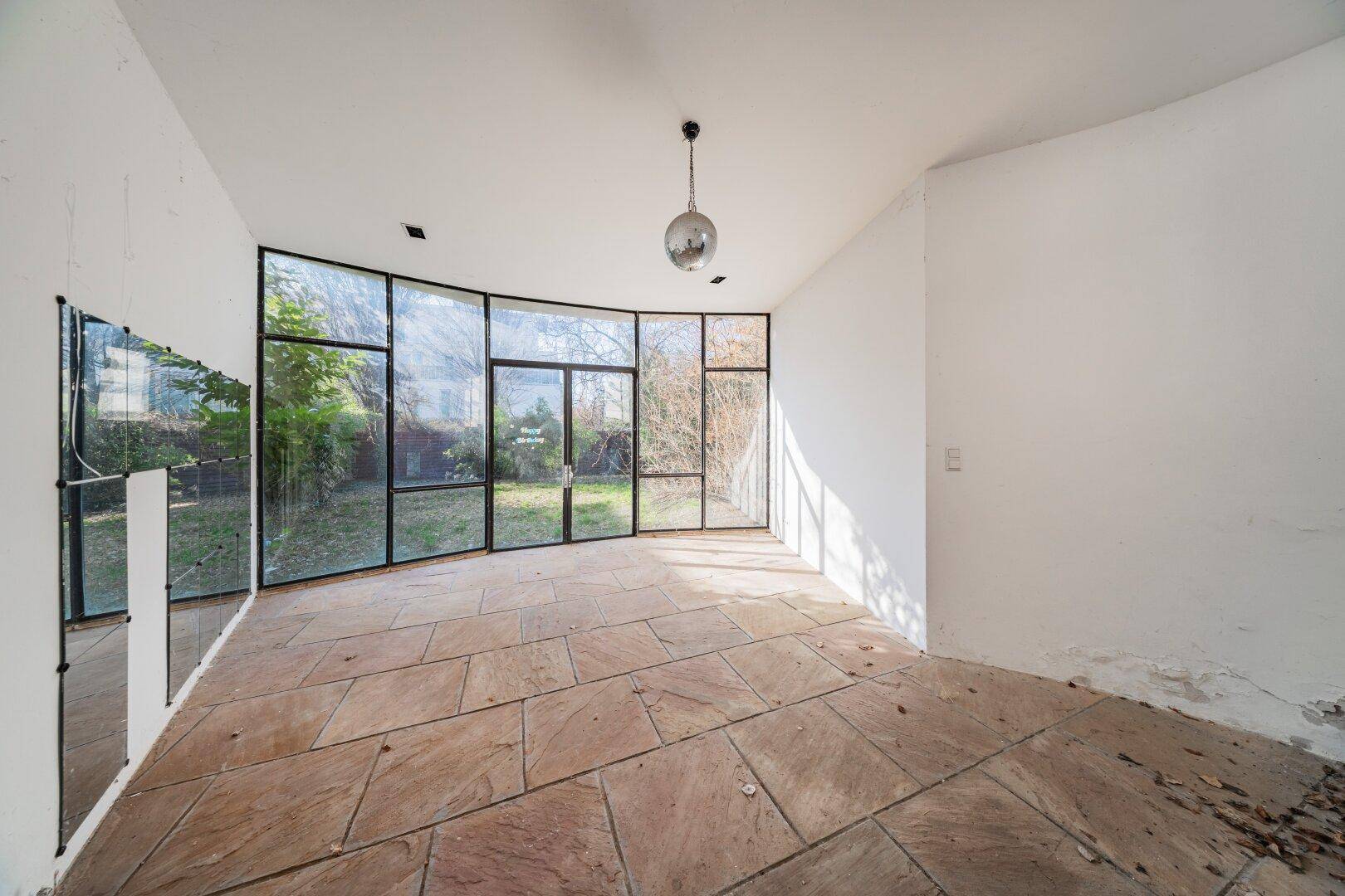 Heller Raum mit gebogener Glasfront, Steinfliesen und direktem Gartenzugang.