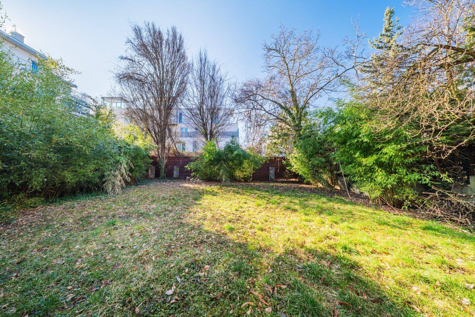 Gepflegter Gartenbereich mit Rasenfläche, Bäumen und Sträuchern.