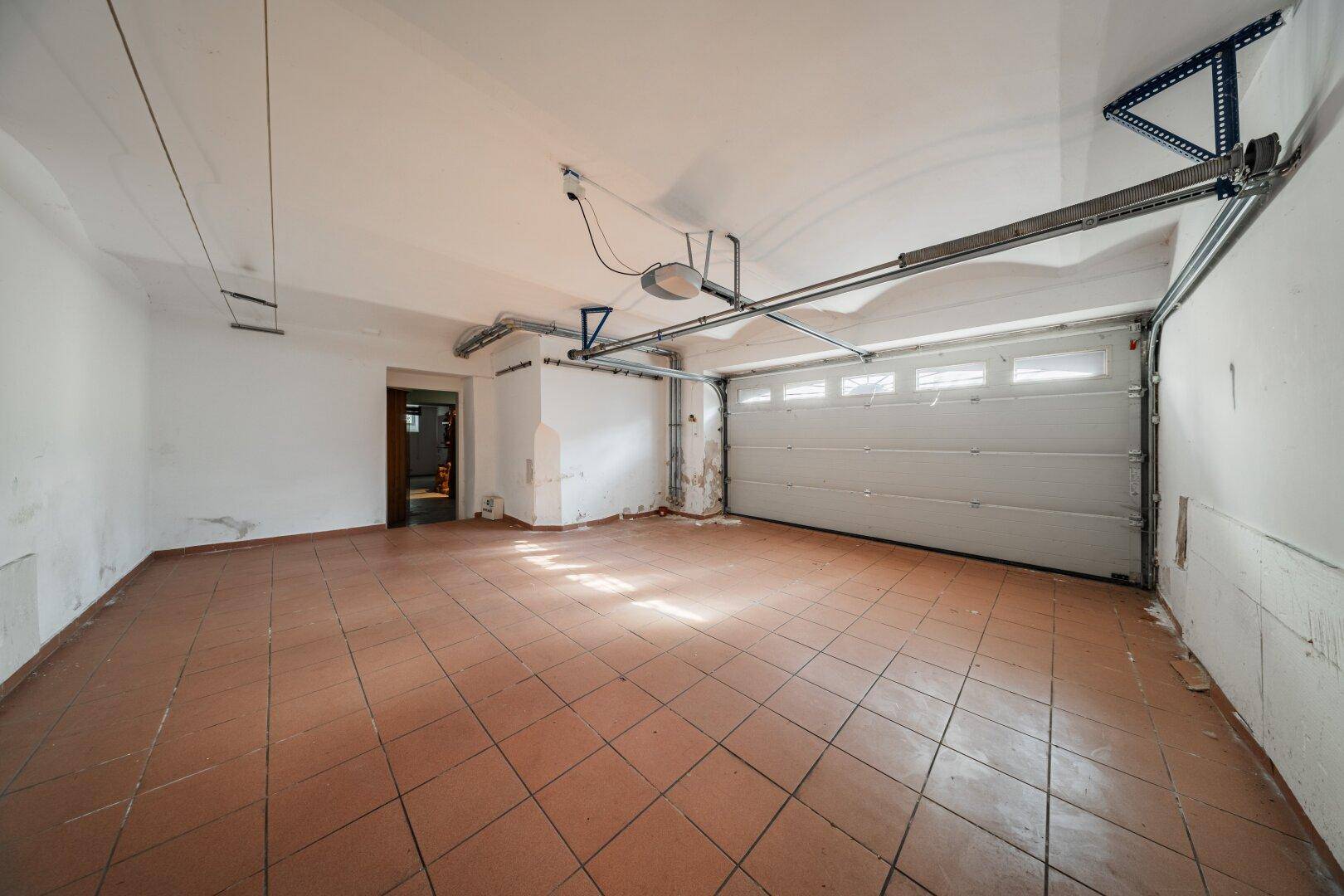 Geräumige Garage mit Fliesenboden und automatischem Garagentor.