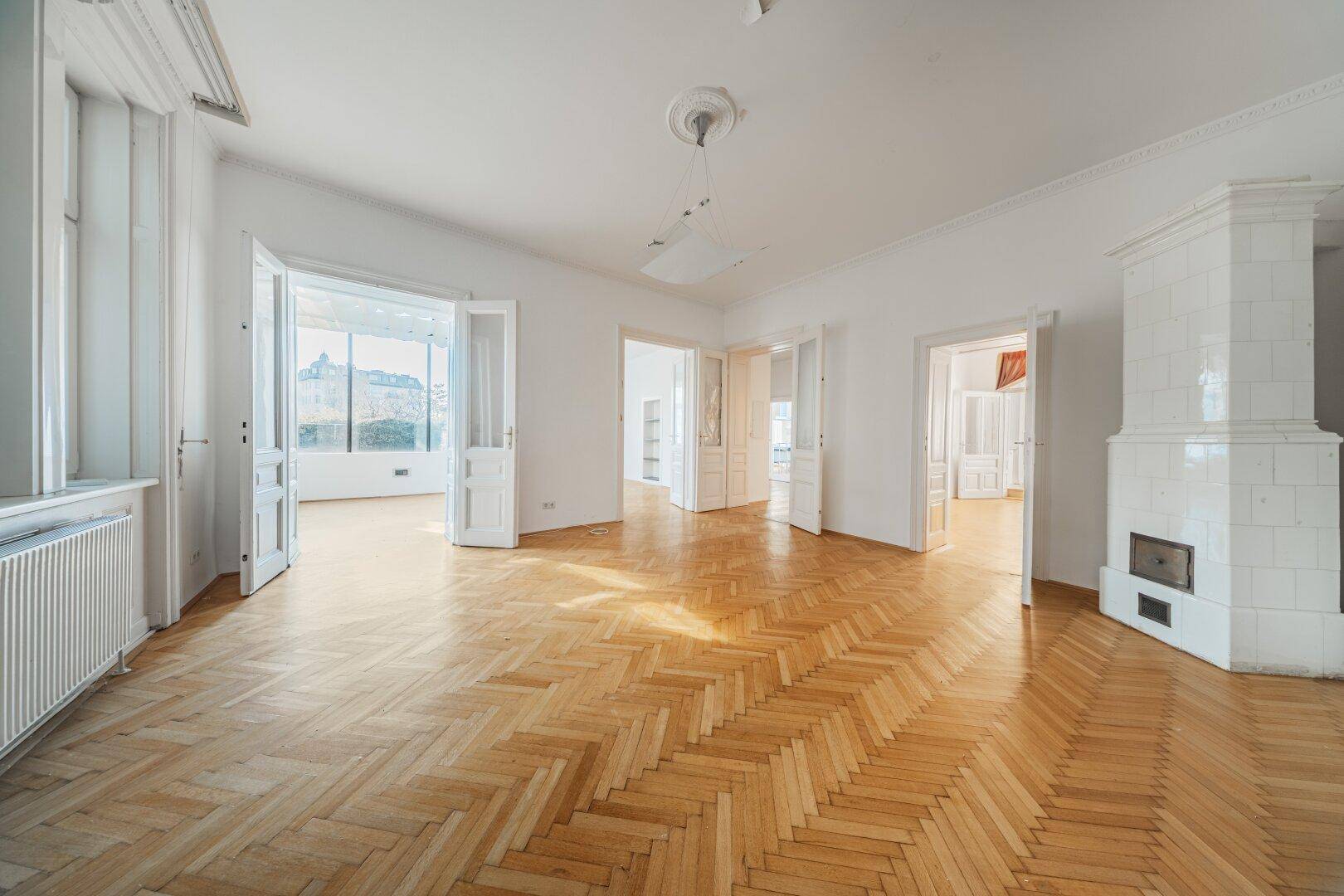 Helles Wohnzimmer mit Fischgrätparkett, hohen Decken und einem traditionellen Kachelofen.