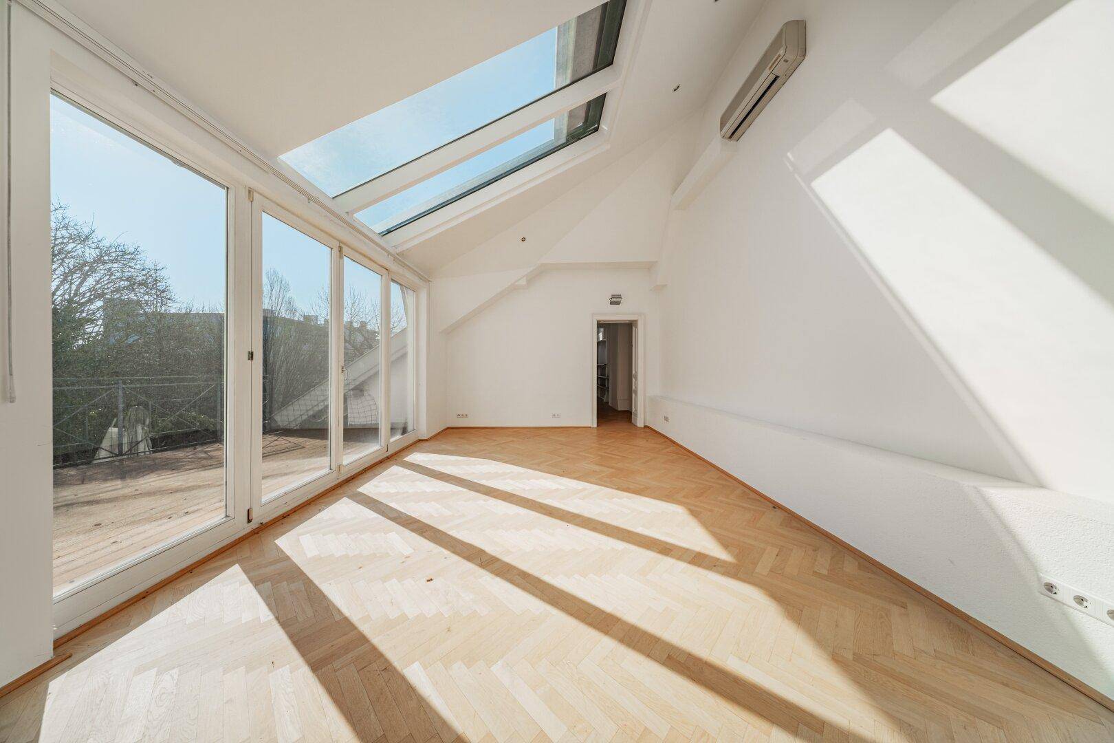Lichtdurchfluteter Dachraum mit Parkettboden, großen Dachfenstern und Zugang zum Balkon.