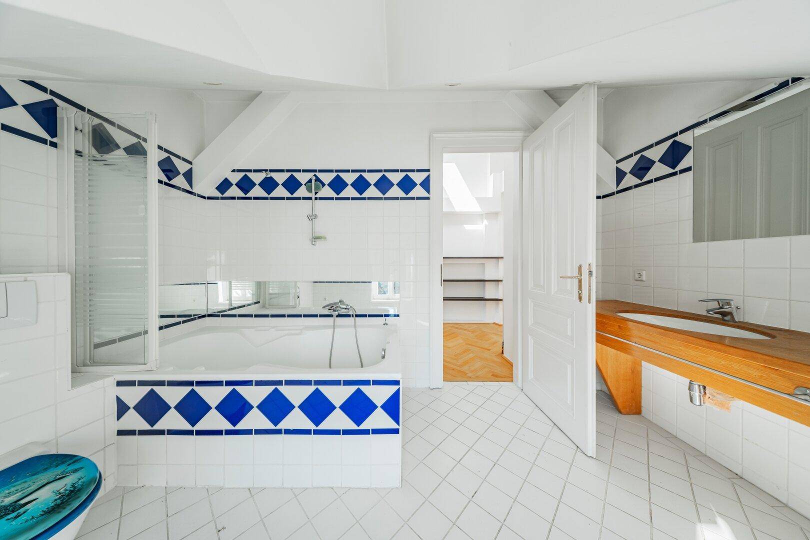 Badezimmer mit blauen und weißen Fliesen, Badewanne und Holzwaschtisch.