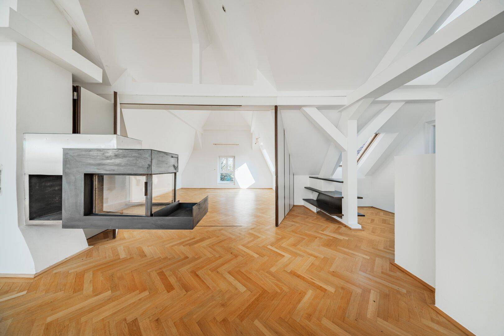 Offener Dachwohnraum mit modernem Kamin, Holzbalken und Fischgrätparkett.