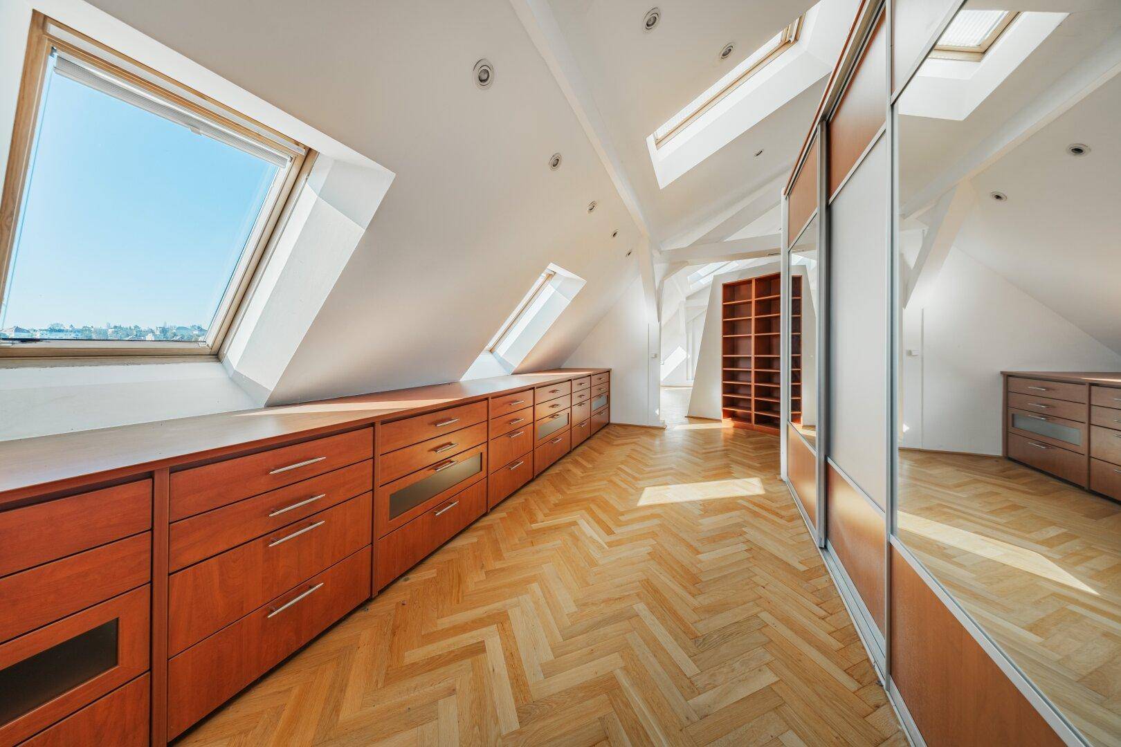 Geräumiges Dachzimmer mit Einbauschränken, Dachfenstern und Fischgrätparkett.