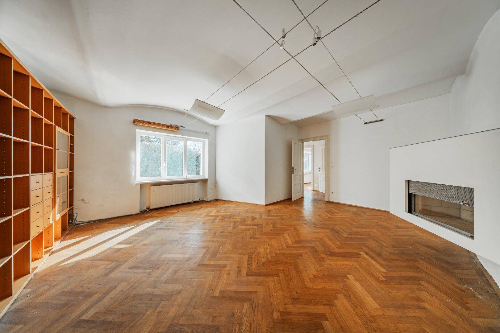 Helles Wohnzimmer mit Parkettboden, integriertem Kamin und großem Bücherregal.