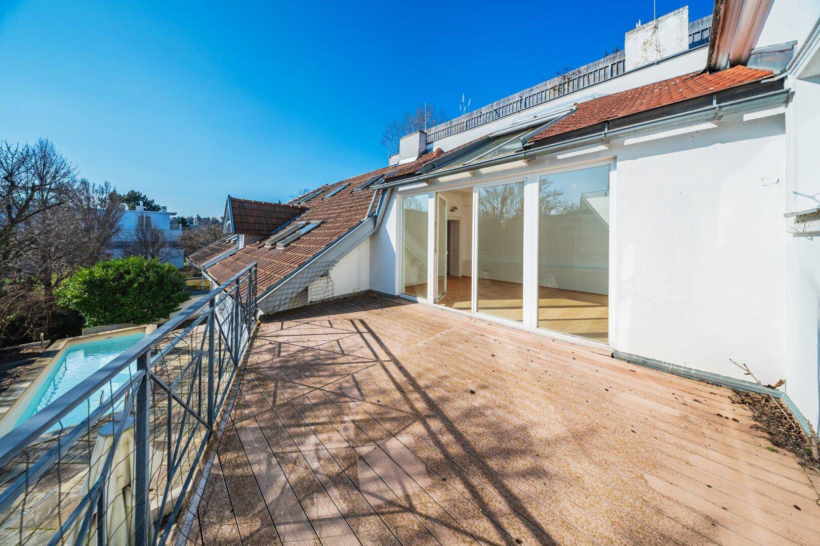 Geräumiger Balkon mit Holzboden, Metallgeländer und Blick auf den Poolbereich.