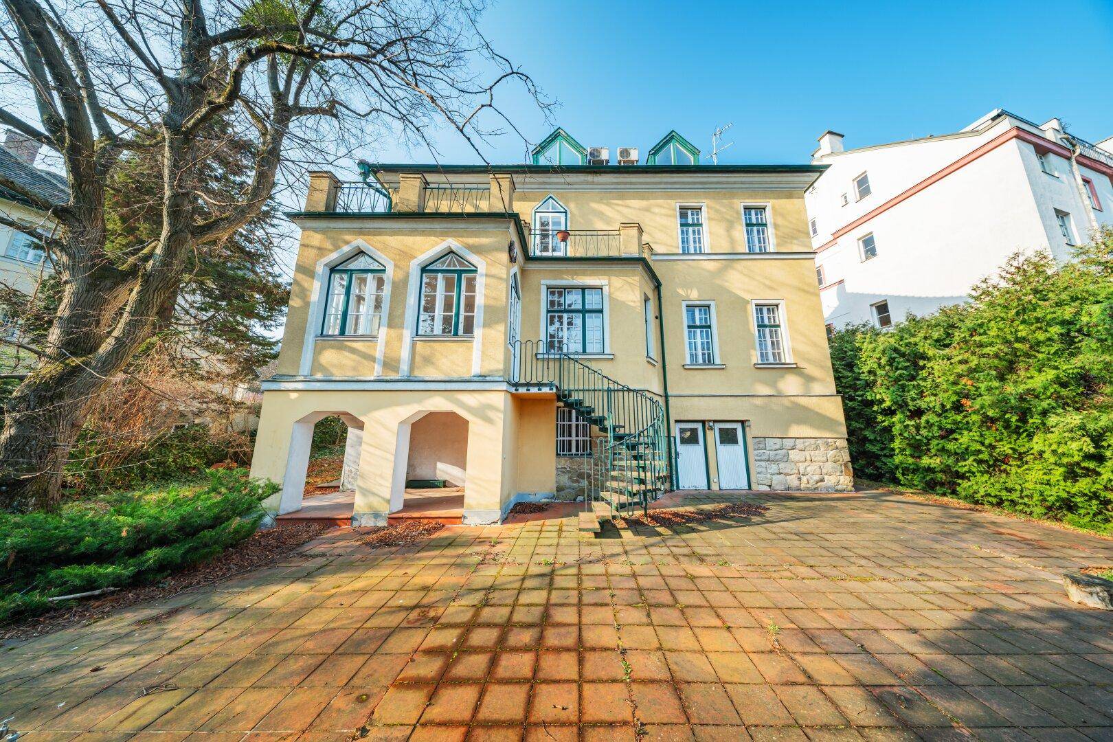 Historisches Gebäude mit gelber Fassade, grünen Akzenten und einer eleganten Außentreppe.