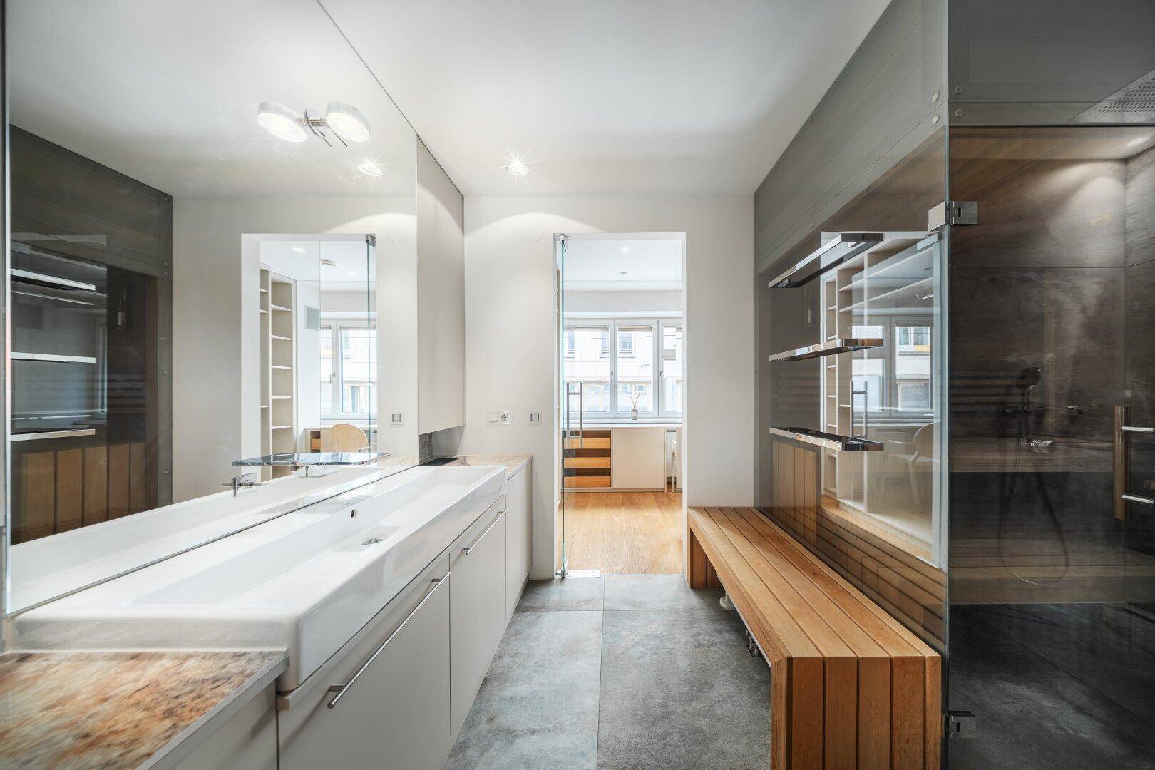 Elegantes Badezimmer mit großem Spiegel, Dusche und Blick in den angrenzenden Raum.