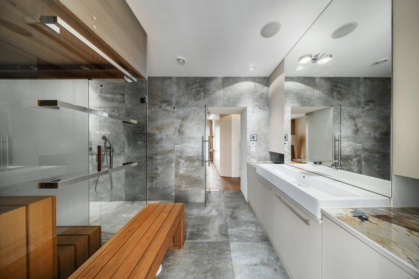 Modernes Badezimmer mit grauen Fliesen, großer begehbarer Dusche und Holzbank.