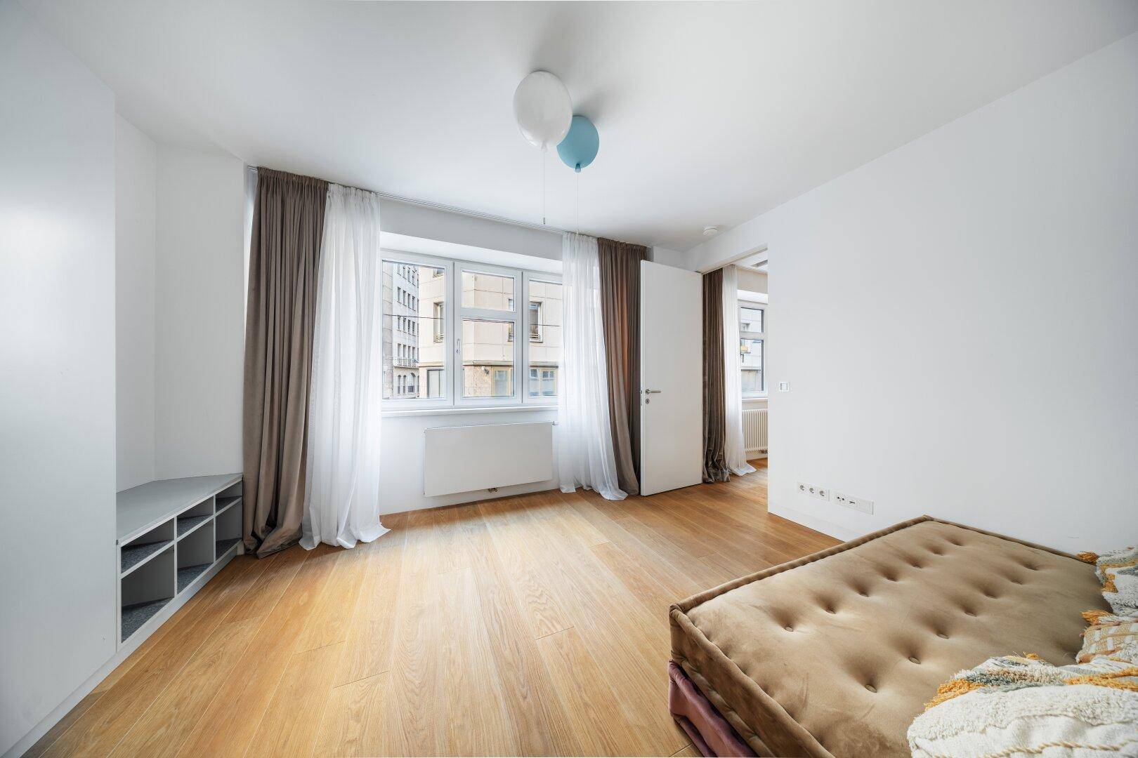 Geräumiges Schlafzimmer mit Holzboden, großen Fenstern und Blick auf die Stadt.