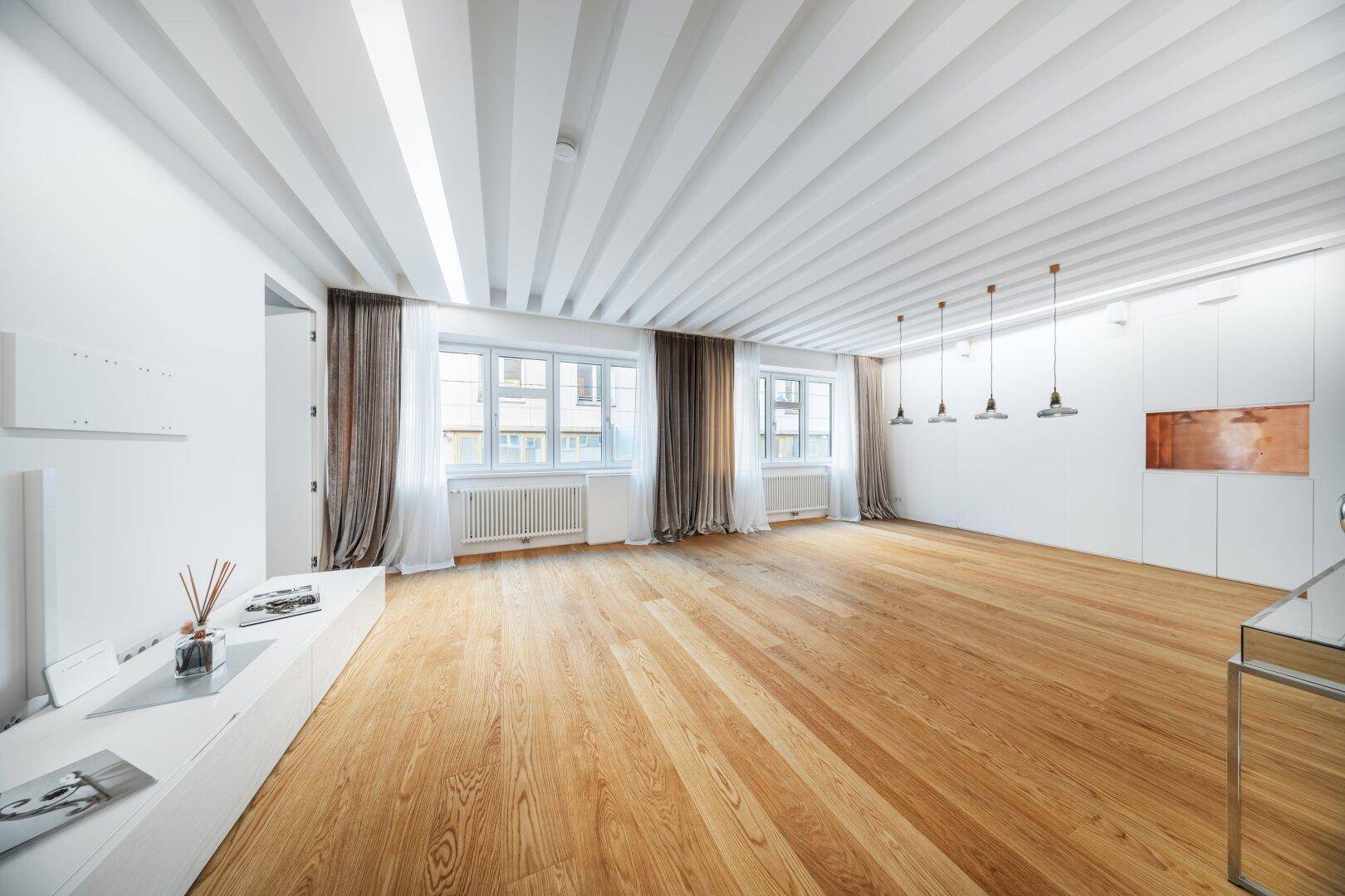 Heller Wohnbereich mit Holzbalkendecke, Parkettboden und moderner Pendelleuchte.