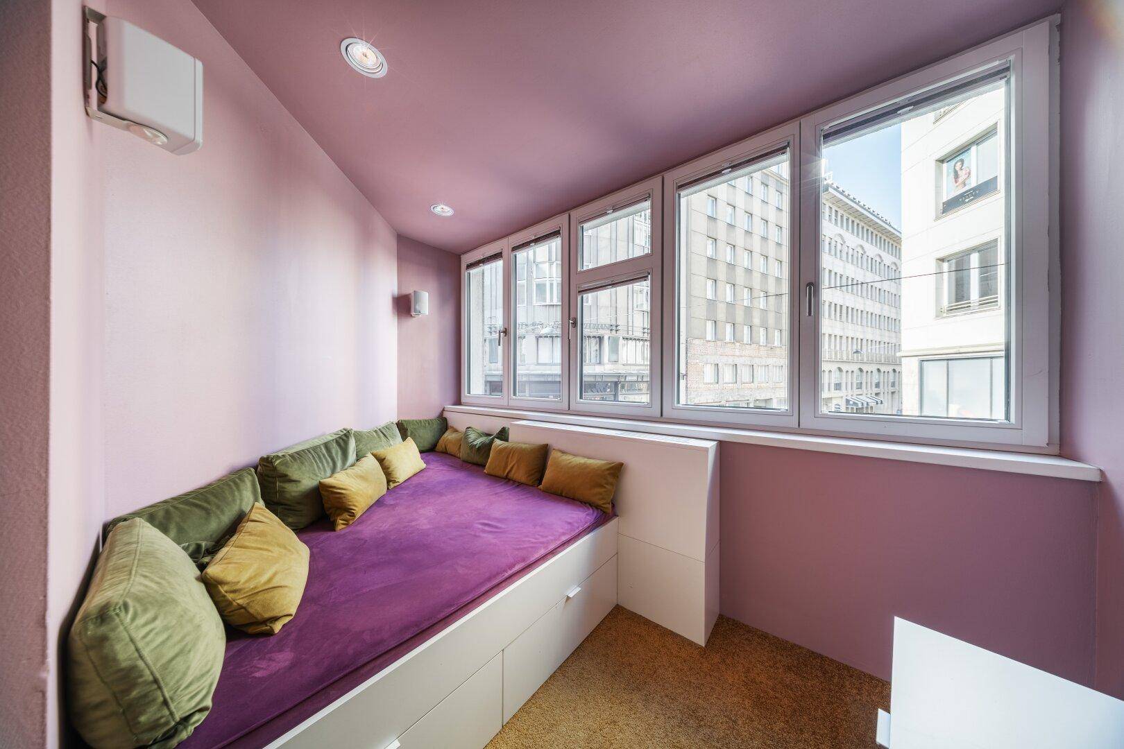Kleines Schlafzimmer mit eingebautem Bett, lila Wänden und Blick auf die Stadt.