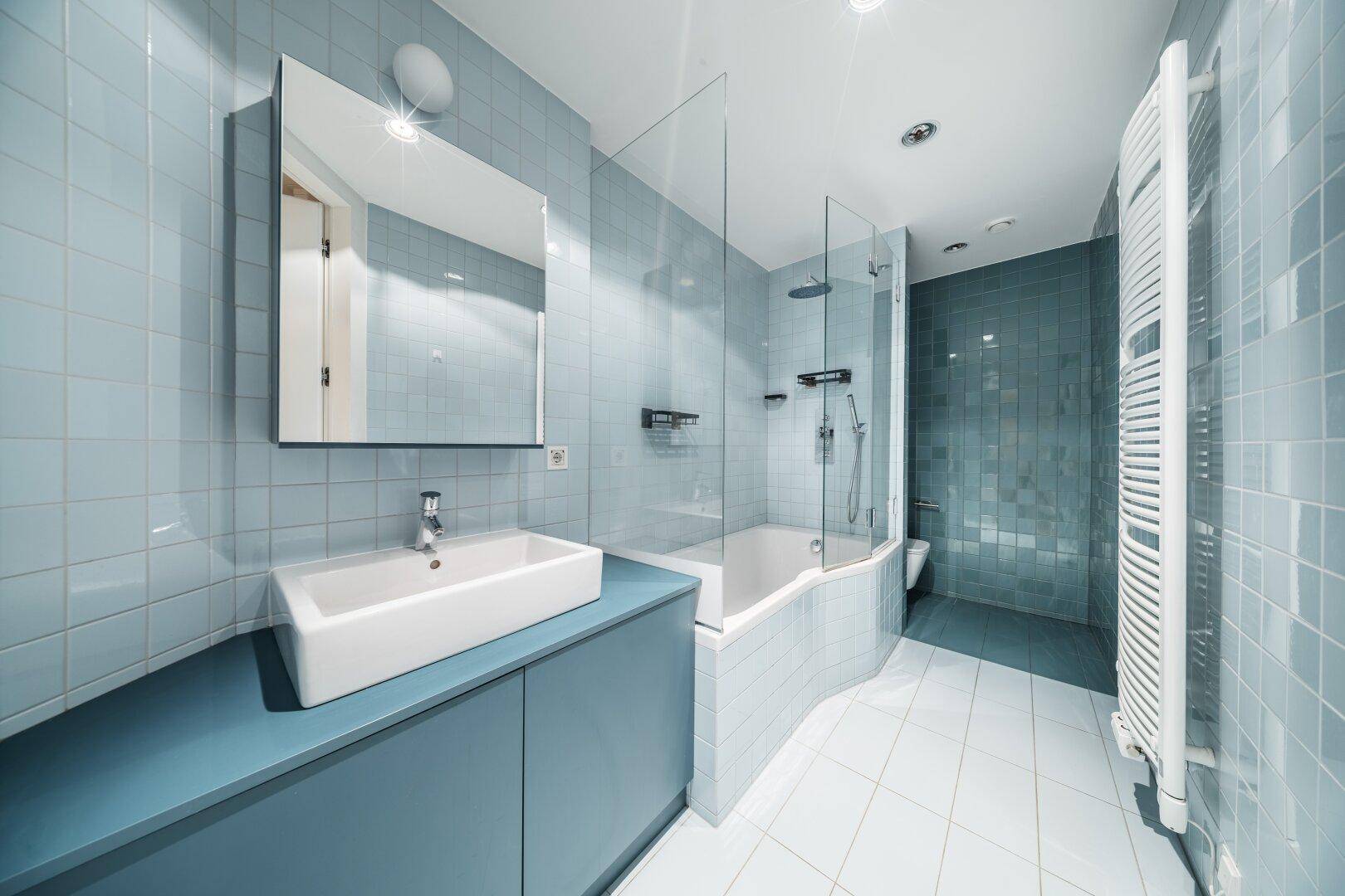Modernes Badezimmer mit blauen Fliesen, Badewanne mit Duschbereich und Handtuchheizkörper.