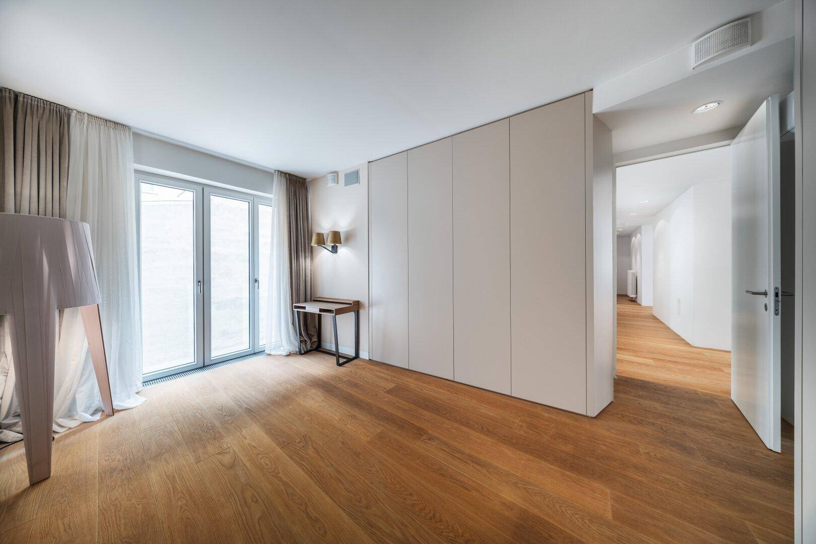 Helles Schlafzimmer mit Holzboden, Einbauschränken und Zugang zu einem Außenbereich.