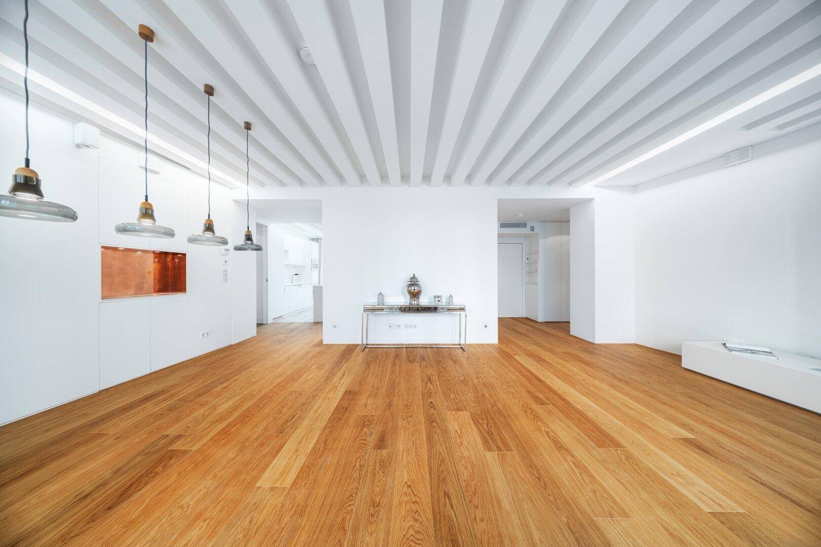 Großzügiger Wohnraum mit Holzbalkendecke, Parkettboden und minimalistischer Einrichtung.