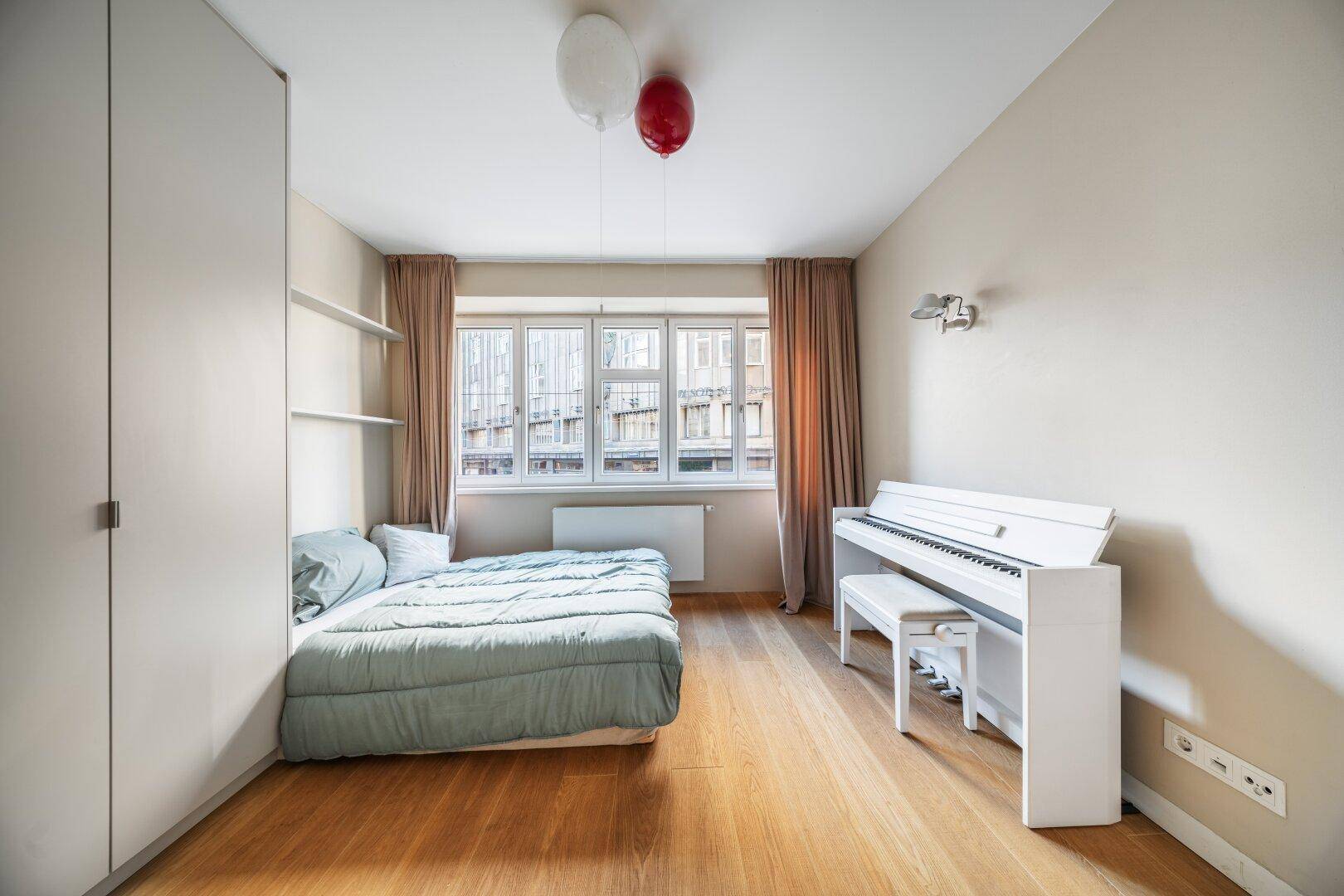 Kinderzimmer mit Holzboden, weißem Klavier und großen Fenstern für viel Tageslicht.