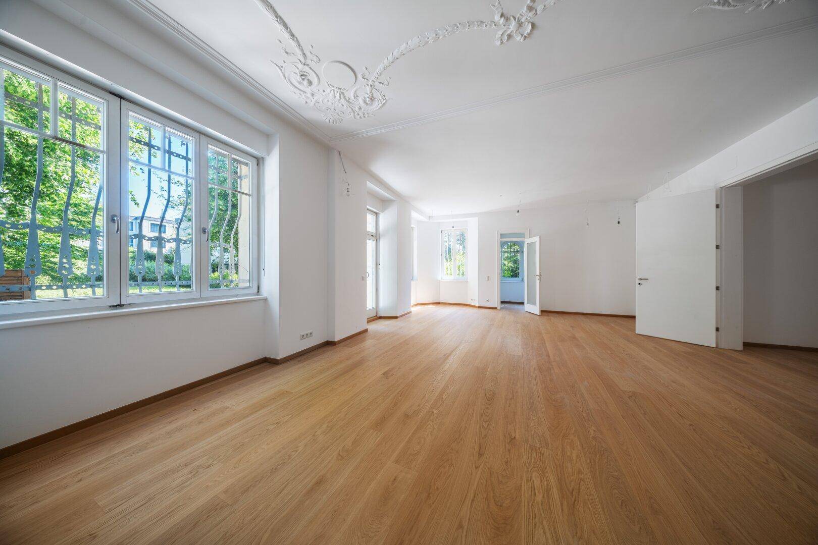 Geräumiges Wohnzimmer mit Eichenparkett, Stuckdecke und großen Fenstern zum Garten.