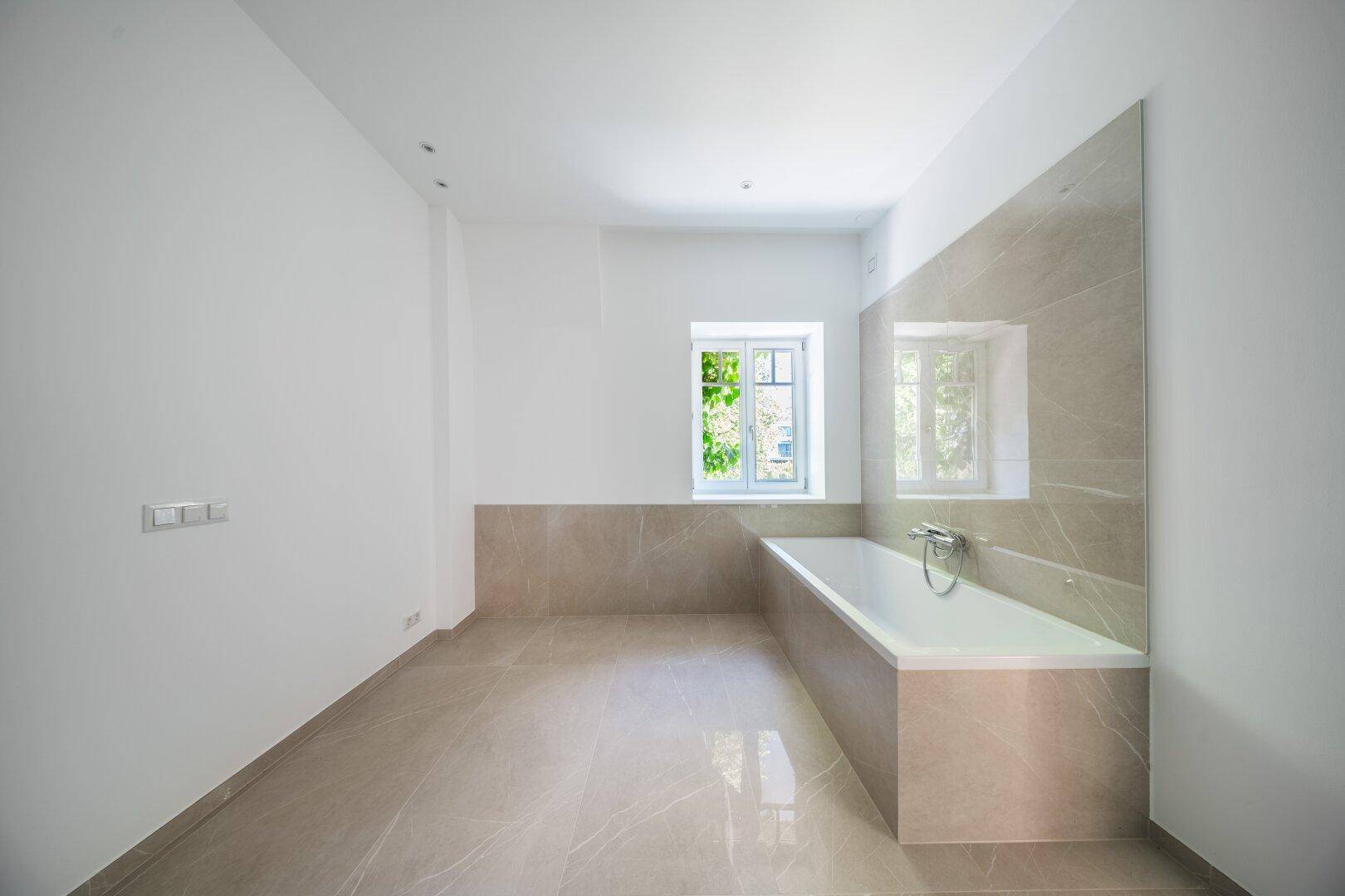Modernes Badezimmer mit Badewanne, großen Fliesen und einem Fenster.