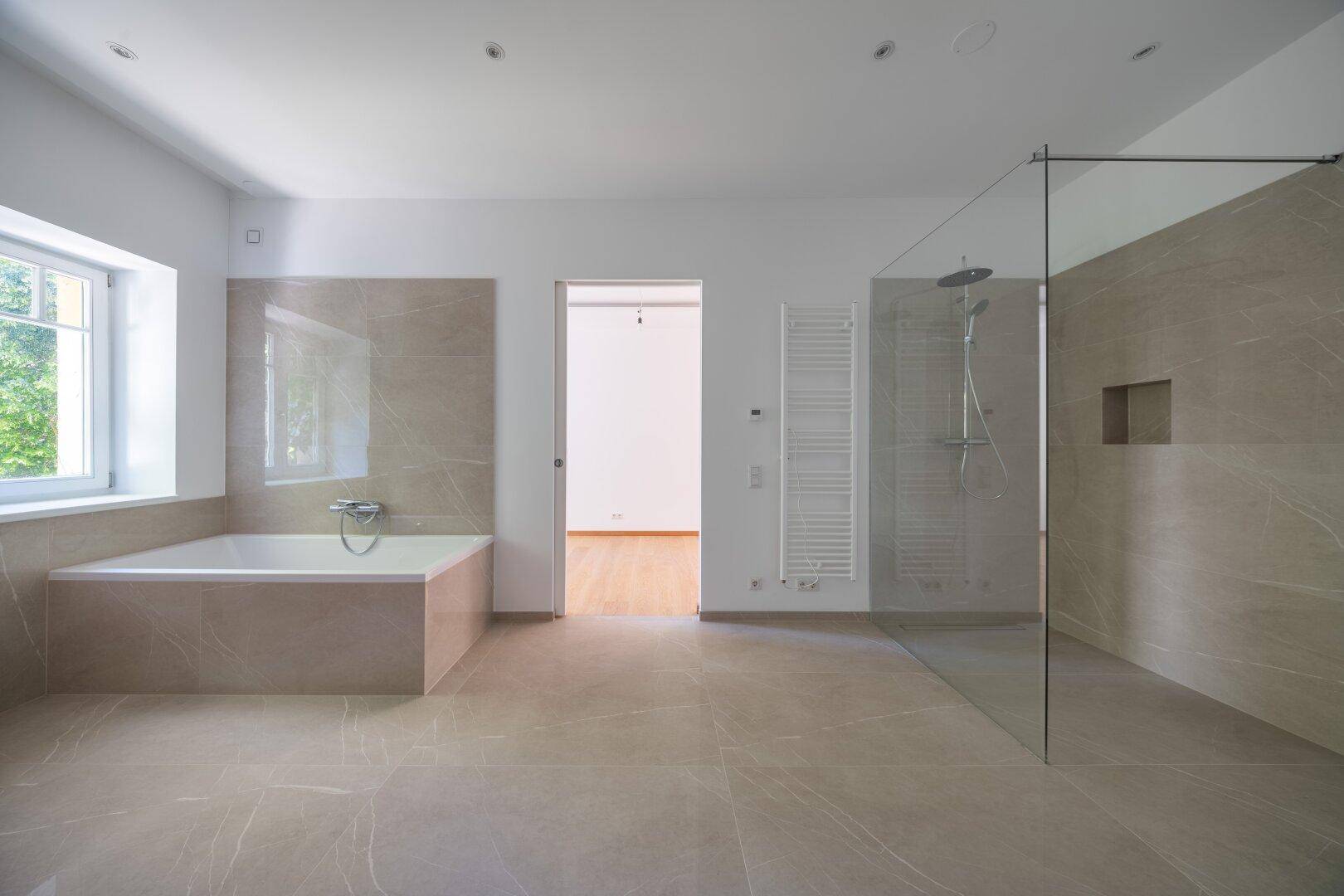 Geräumiges Badezimmer mit Badewanne, großer Dusche und beheiztem Handtuchhalter.
