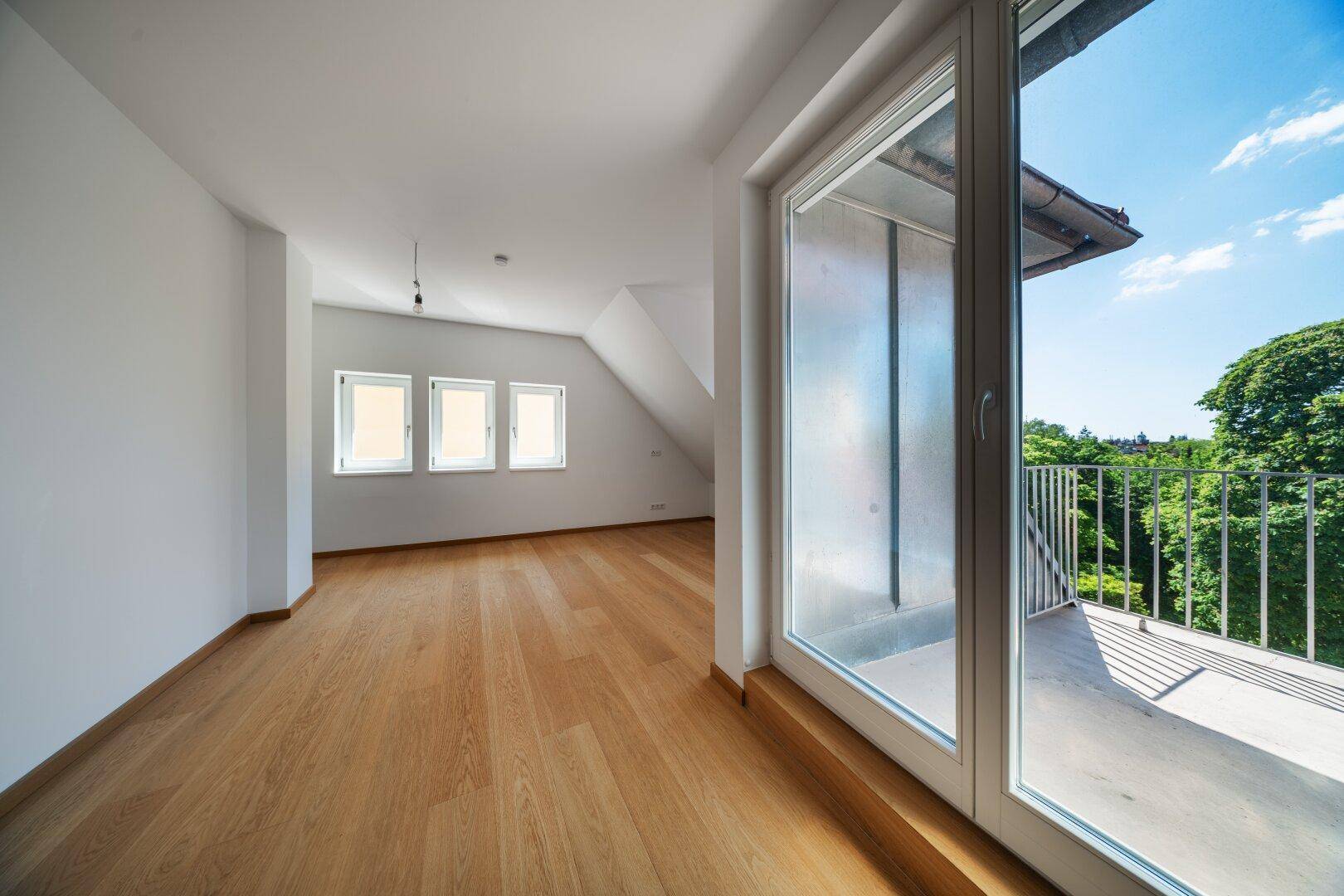 Helles Zimmer mit Eichenparkett, Dachschräge und Zugang zu einem Balkon mit Weitblick.