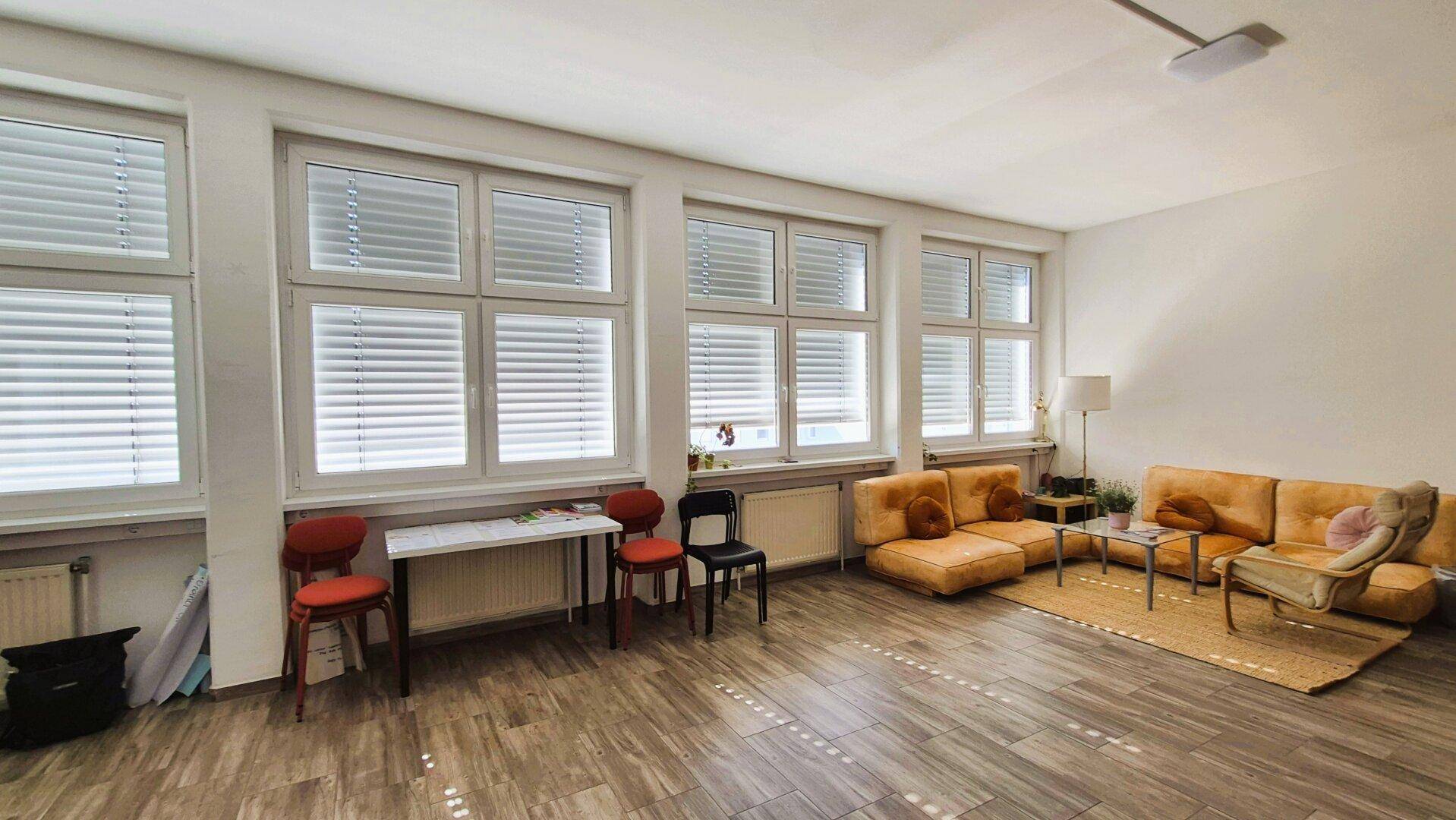 Geräumiger Wohnbereich mit großen Fenstern, Jalousien und bequemen orangefarbenen Sofas auf Holzboden.