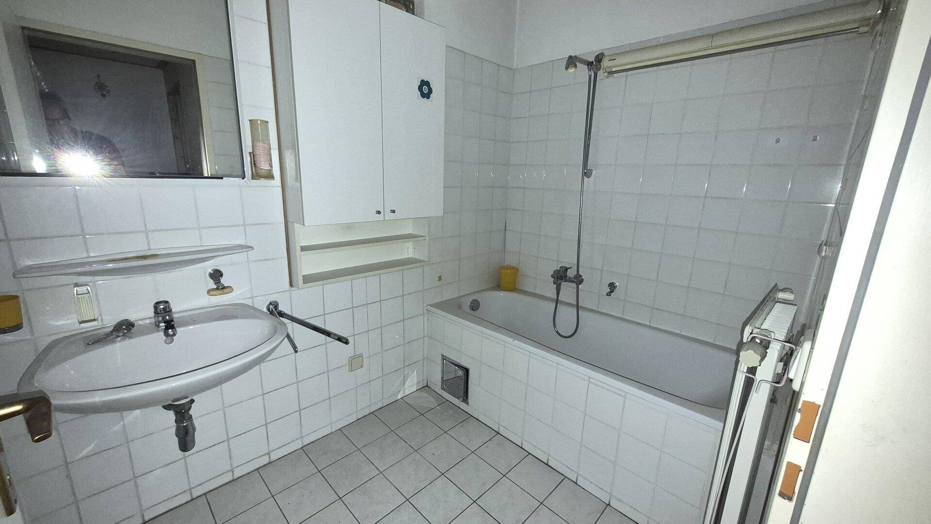 Funktionales Badezimmer mit weißen Fliesen, Badewanne und Waschbecken im älteren Stil.