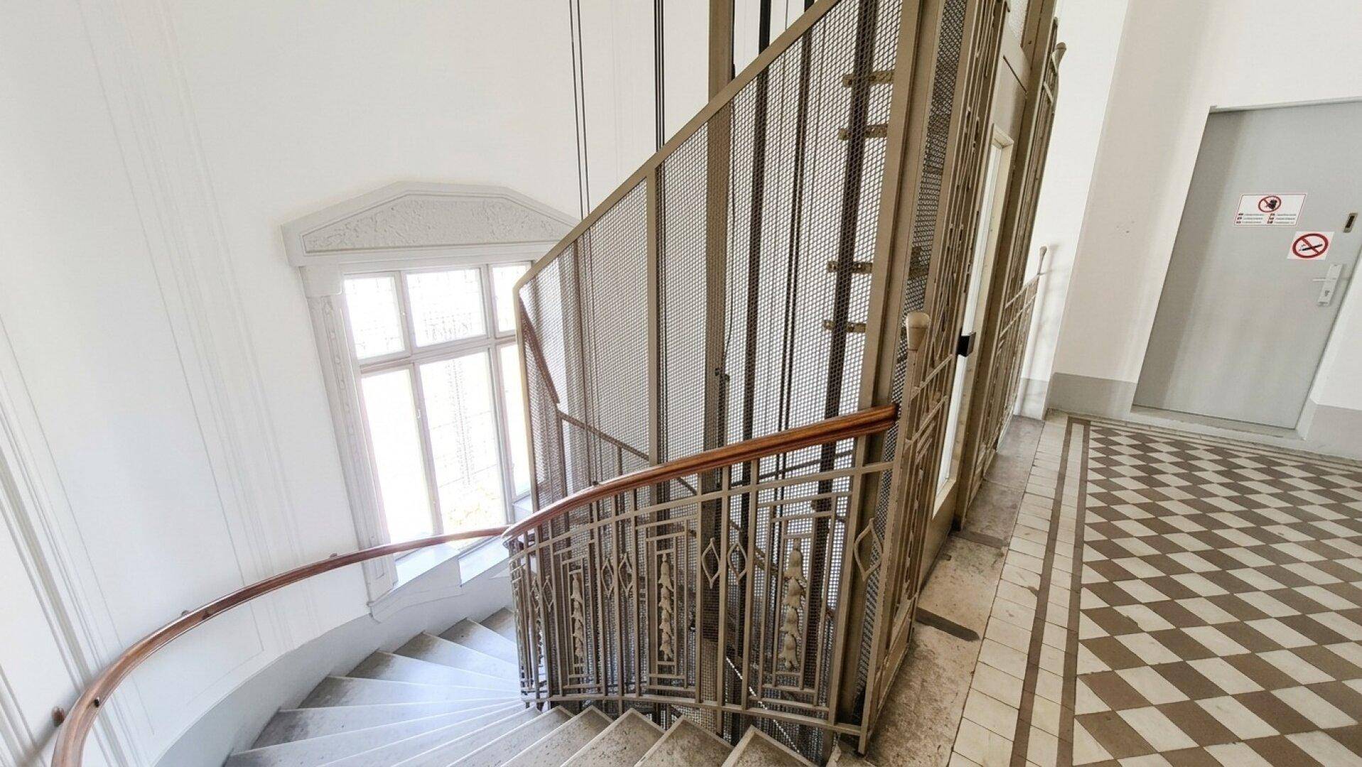 Historisches Treppenhaus mit kunstvollem Geländer und einem Aufzug in einem Altbau.