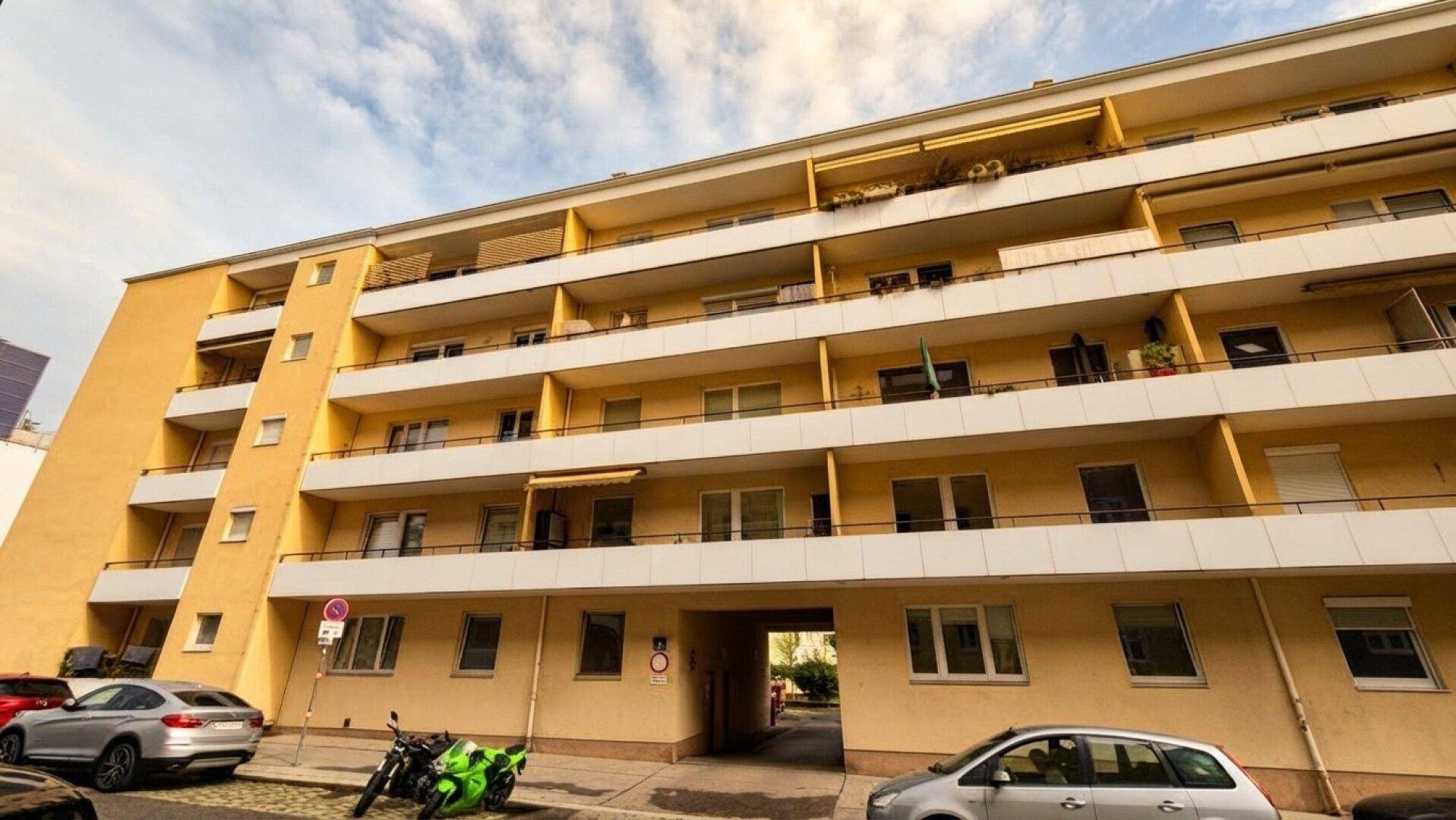 Mehrstöckiges Wohngebäude mit gelber Fassade und zahlreichen Balkonen an einer städtischen Straße.