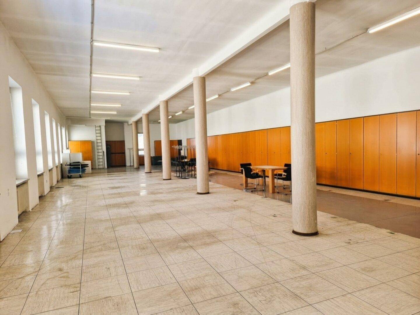 Heller, offener Büroraum mit hohen Decken, Säulen und durchgehenden Holzschränken entlang der Wand, ideal für Teams.
