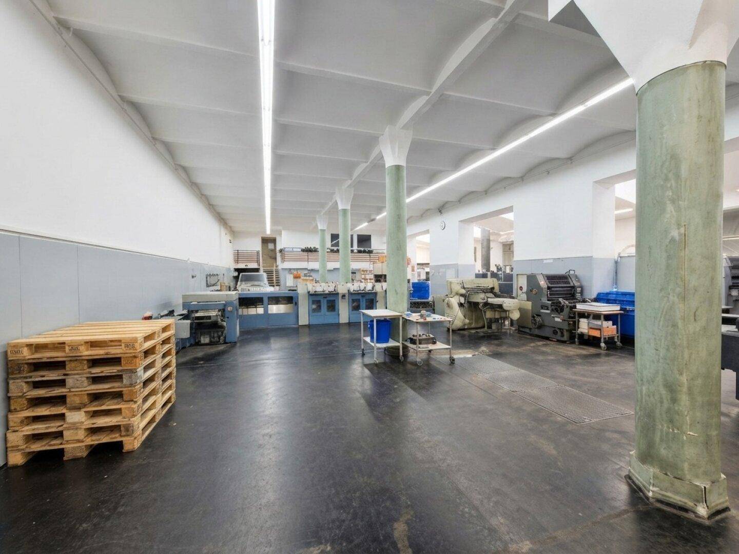 Industrielle Produktionshalle mit Maschinen, Betonboden und tragenden Säulen.