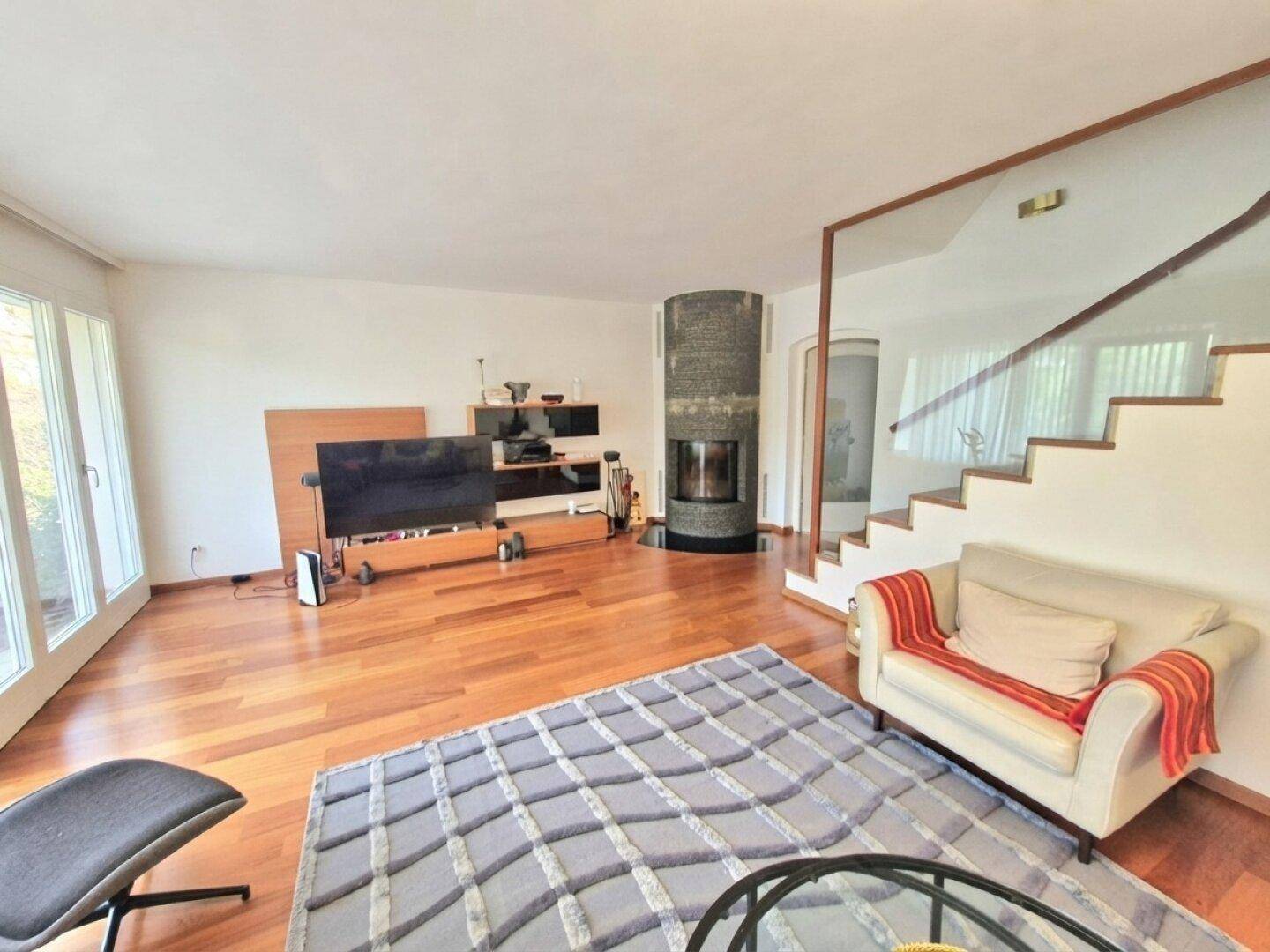 Geräumiges Wohnzimmer mit modernem Kamin, Holzboden und Zugang zur Treppe.