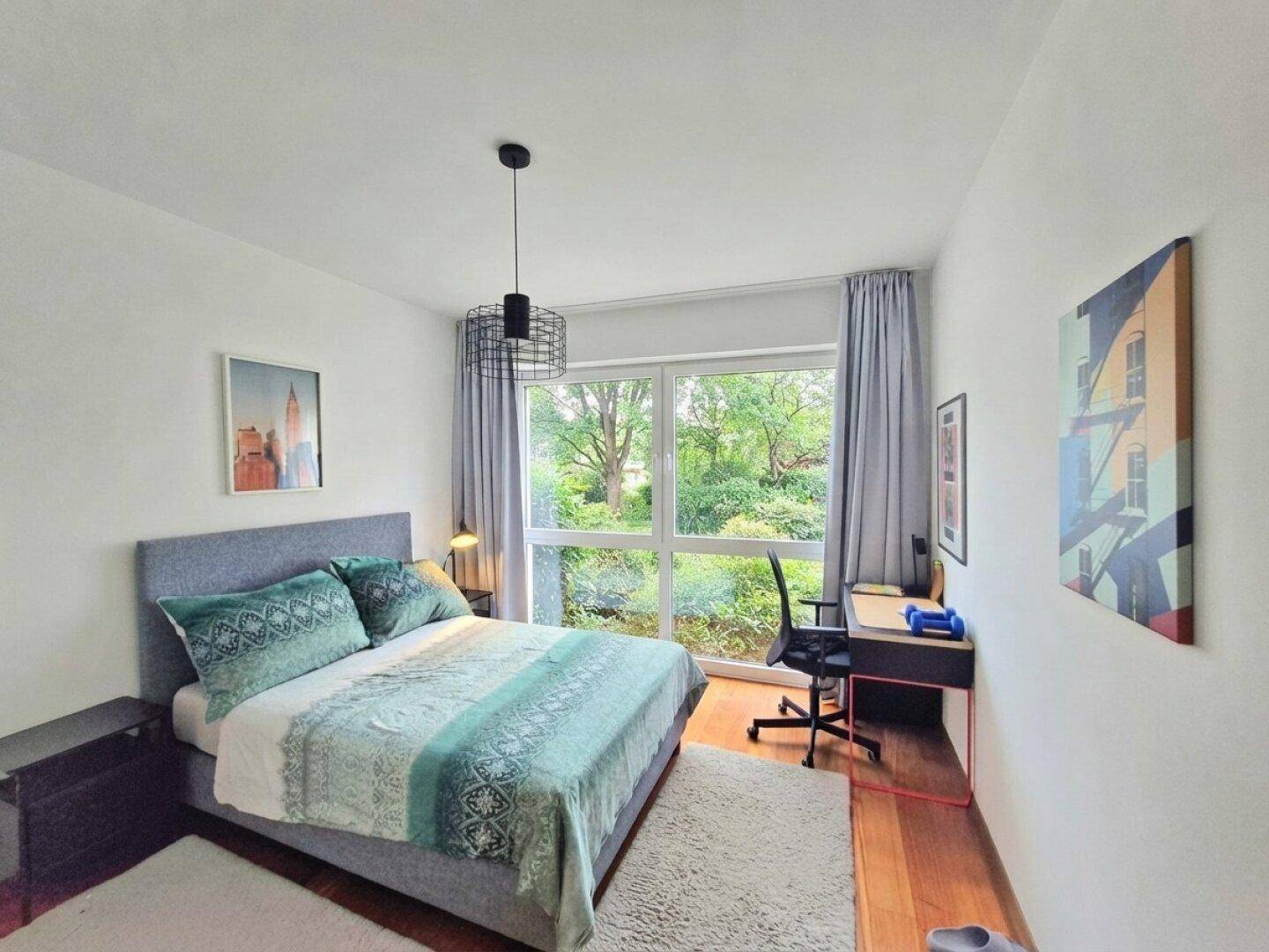 Helles Schlafzimmer mit Bett, Schreibtisch am Fenster und angenehmem Blick ins Grüne.