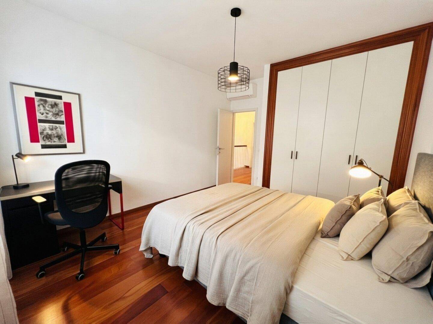 Schlafzimmer mit Holzboden, Schreibtisch und praktischen Einbauschränken.