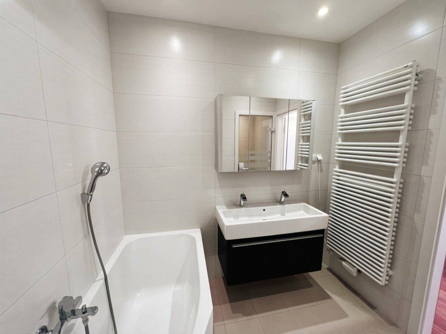 Helles Badezimmer mit Badewanne, Doppelwaschbecken und beheiztem Handtuchhalter.