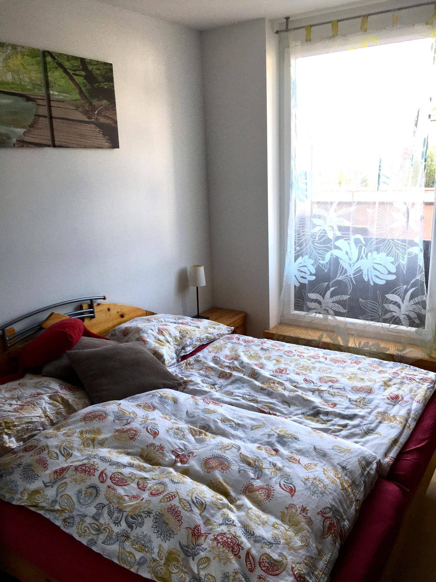 Schlafzimmer mit Doppelbett, Holzboden und großem Fenster für viel Helligkeit.