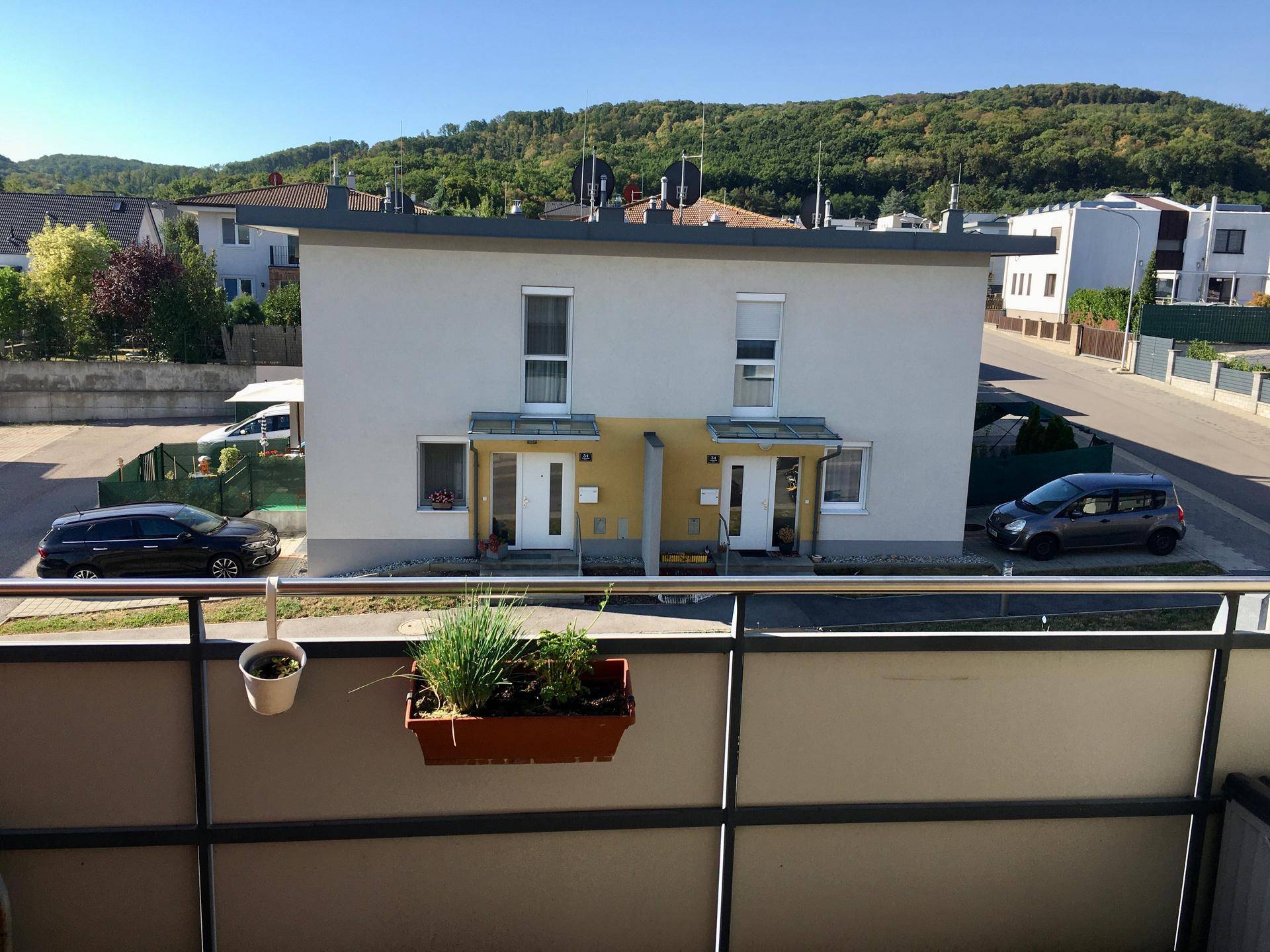 Ansicht eines modernen Doppelhauses mit Flachdach und grüner Hügellandschaft im Hintergrund.