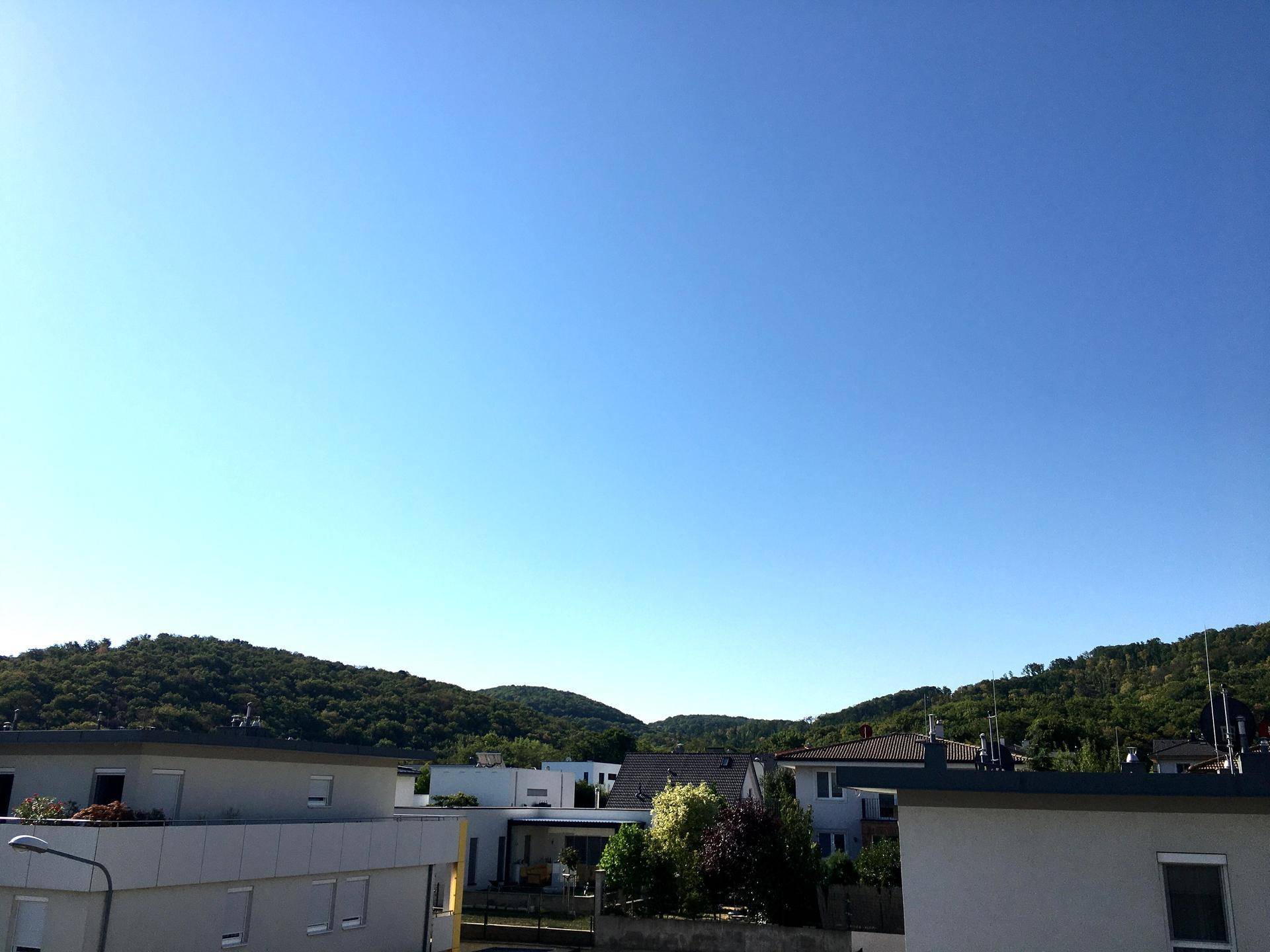 Weitläufiger Blick auf grüne Hügel und den blauen Himmel über der Wohnsiedlung.