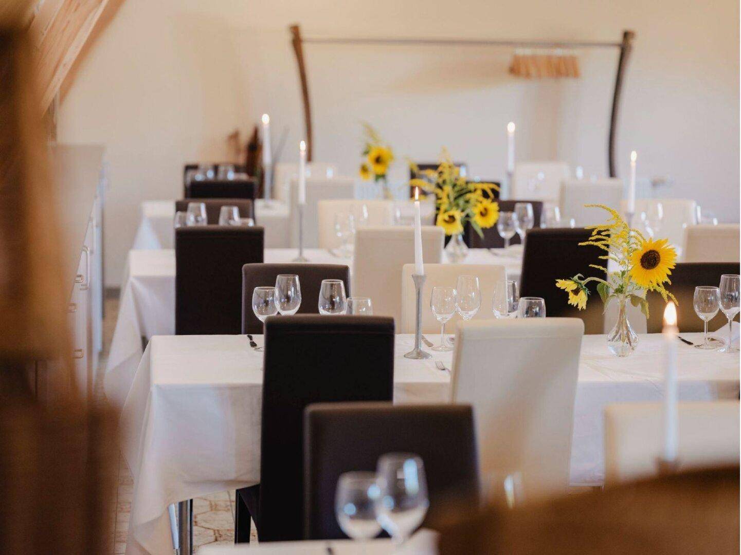 Festlich gedeckte Tische mit weißen Tischdecken, eleganten Stühlen und Sonnenblumen-Dekoration.