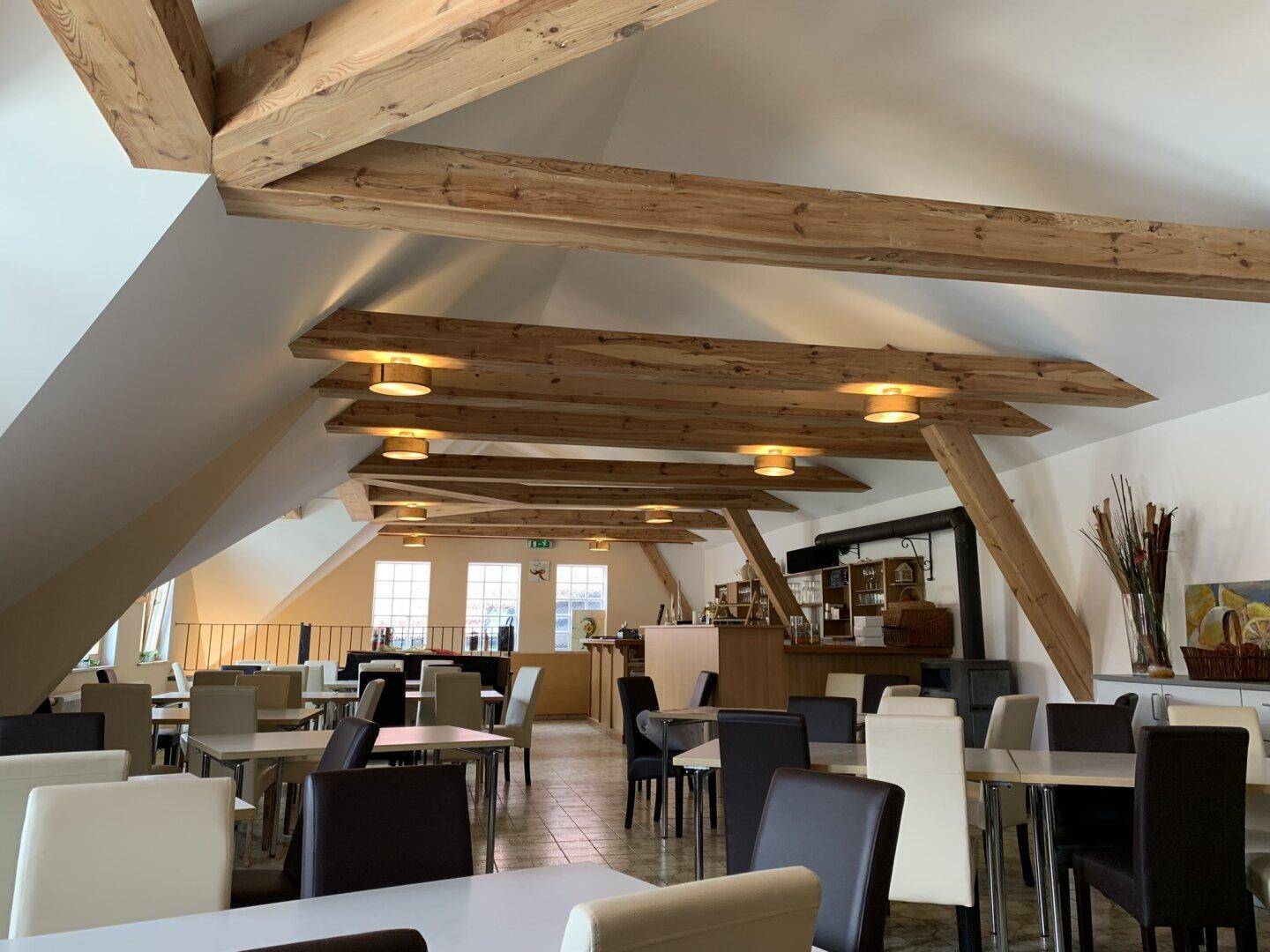 Heller Dachgeschossraum mit Holzbalken und vielen Sitzgelegenheiten, ideal für Gastronomie.