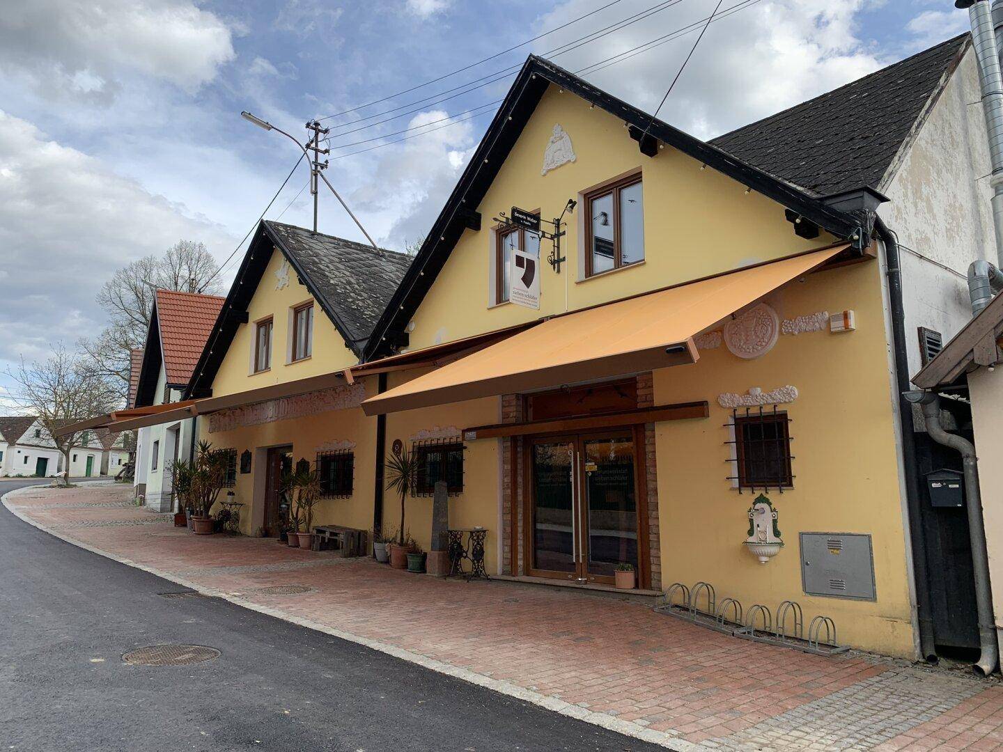 Gelbes Gebäude mit Markisen und traditioneller Architektur an einer ruhigen Dorfstraße.