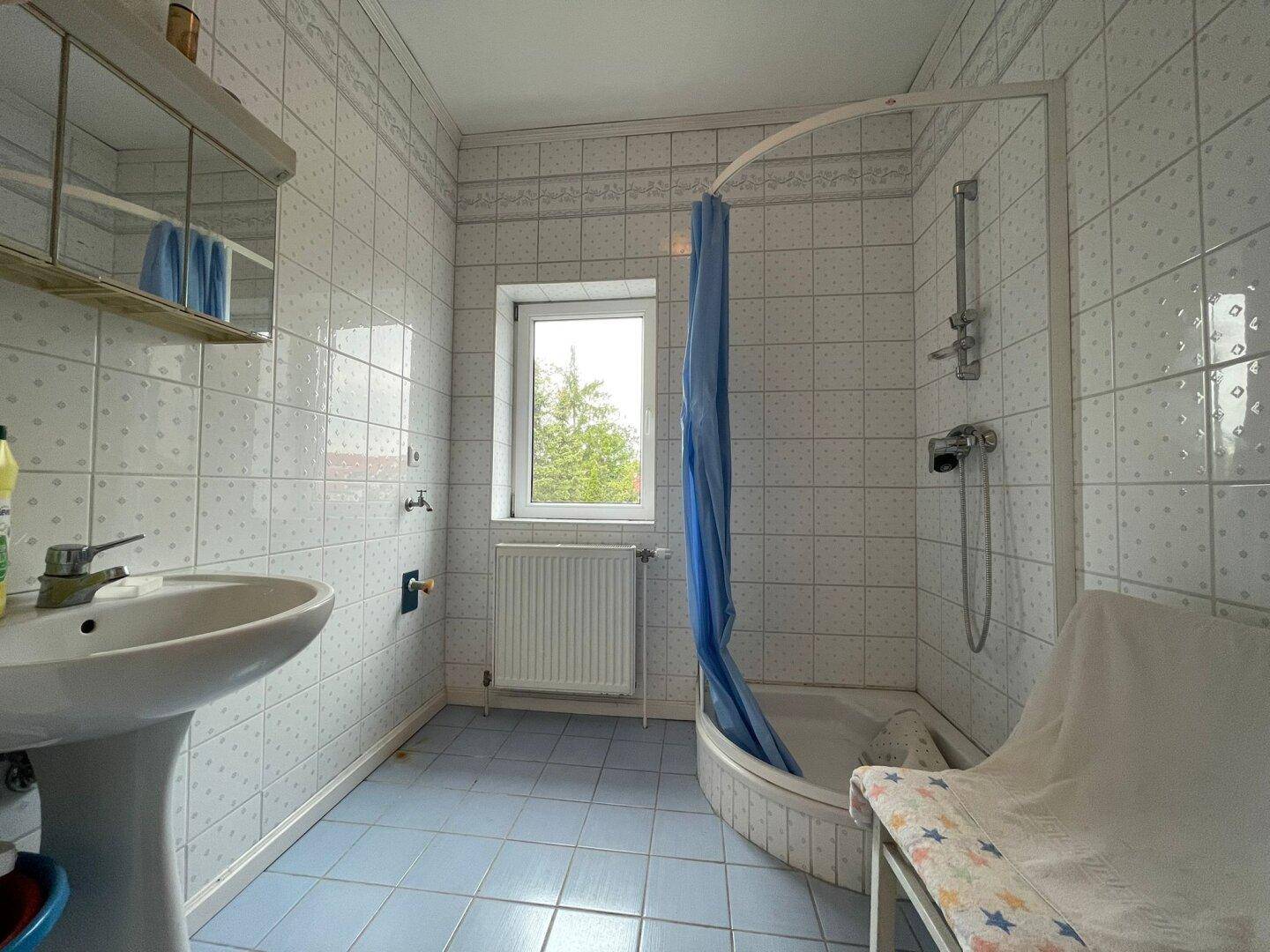 Badezimmer mit hellblauen Fliesen, einer Duschkabine und einem Fenster für natürliche Belüftung.