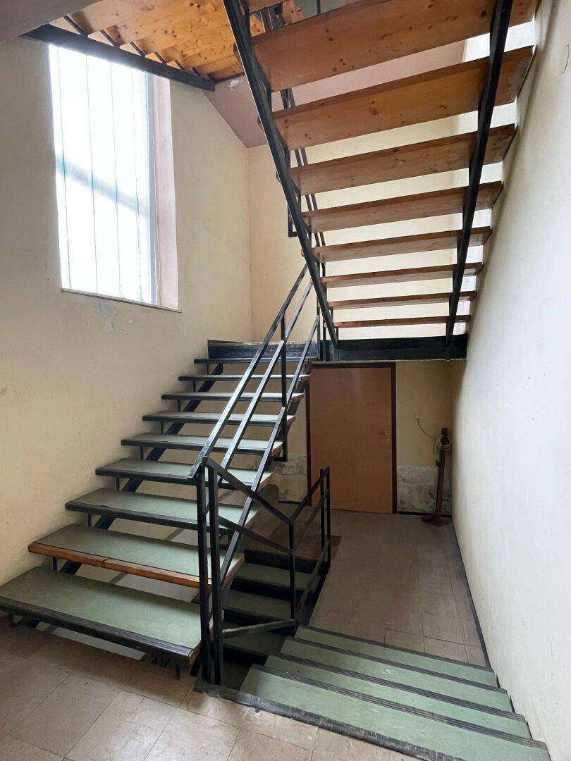 Treppenhaus mit Holzstufen und einem Metallgeländer, das in die oberen Stockwerke führt.