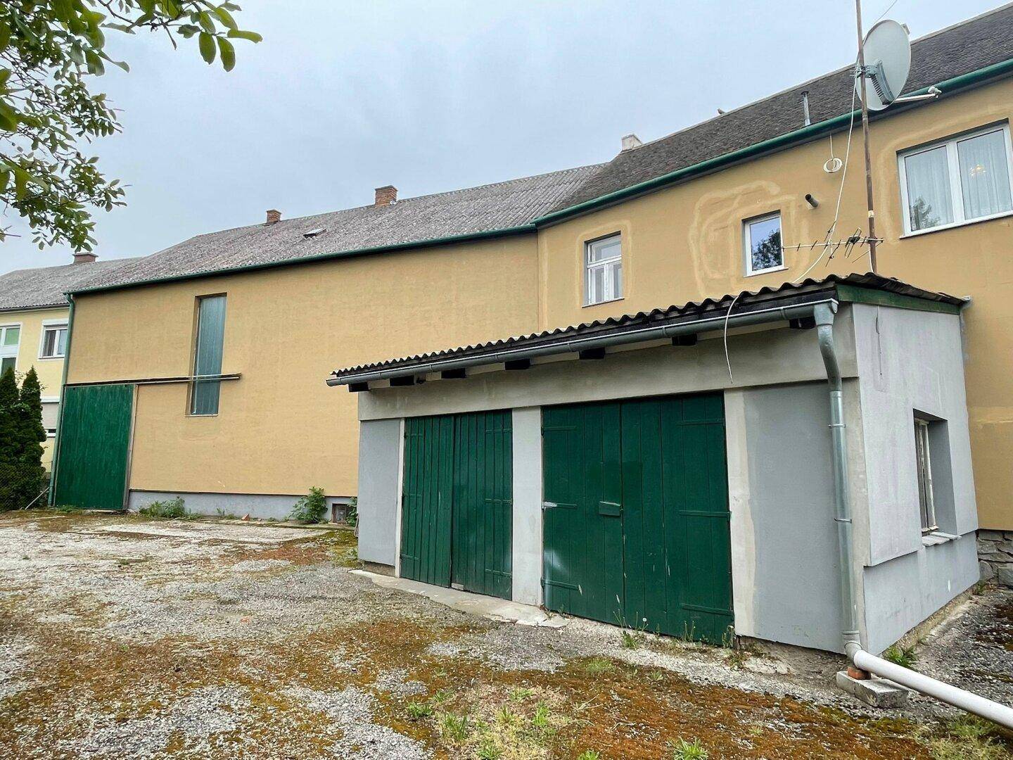 Seitenansicht des Gebäudes mit Garagenanbau und ungenutzter Hoffläche, die Renovierung benötigt.