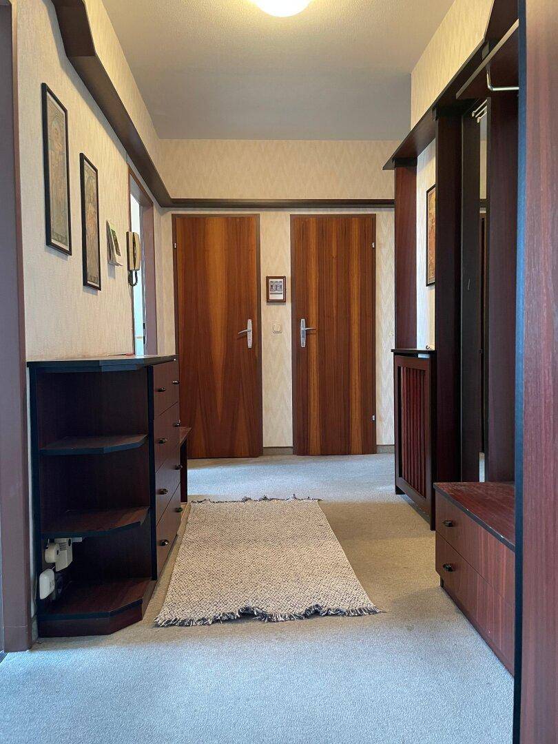 Heller Flur mit Teppichboden und praktischen Holzmöbeln, der zu den weiteren Räumen führt.