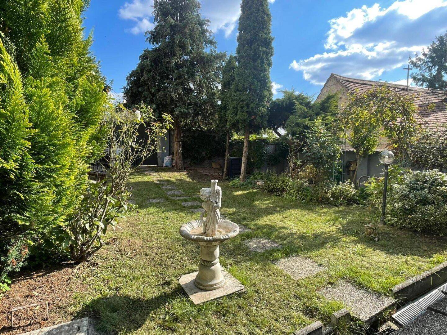 Gepflegter Garten mit Rasenfläche, Bäumen und einer dekorativen Steinfigur im Zentrum.